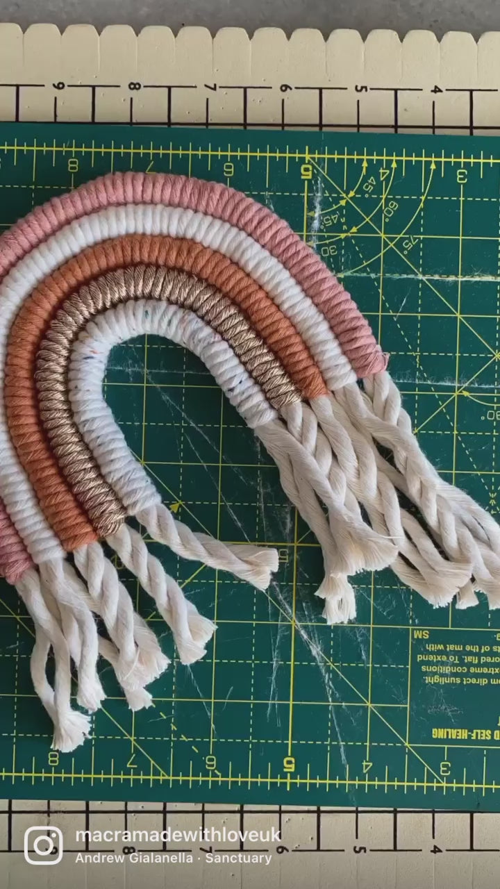 A video showing part of the making process of a macrame rainbow in shades of pink.