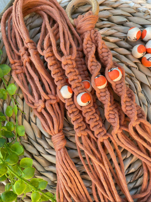 A handmade macrame plant hanger, made with terracotta coloured recycled cotton and a repurposed wooden hanging ring, with 4 wooden pumpkin patterned beads.