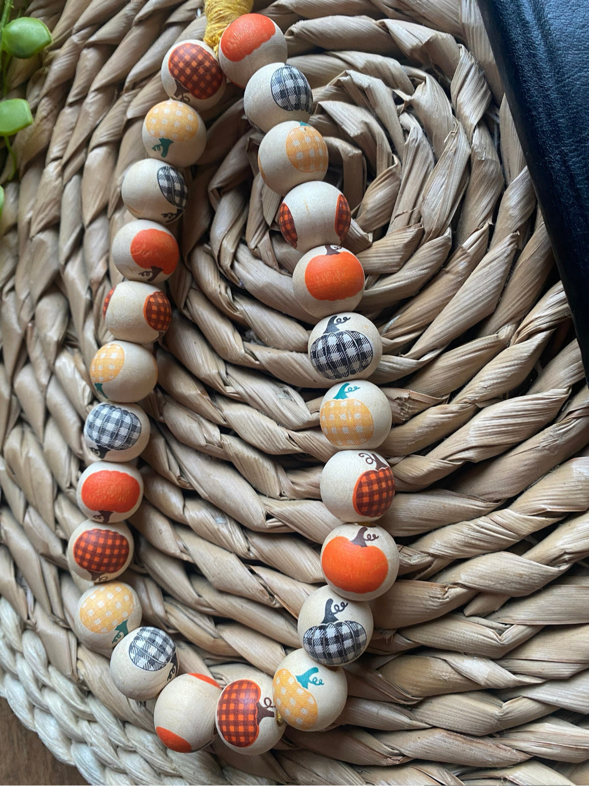 Close up of a handmade wristlet phone charm, made with pumpkin patterned wooden beads on a wicker woven placemat next to a black wallet style phone case.