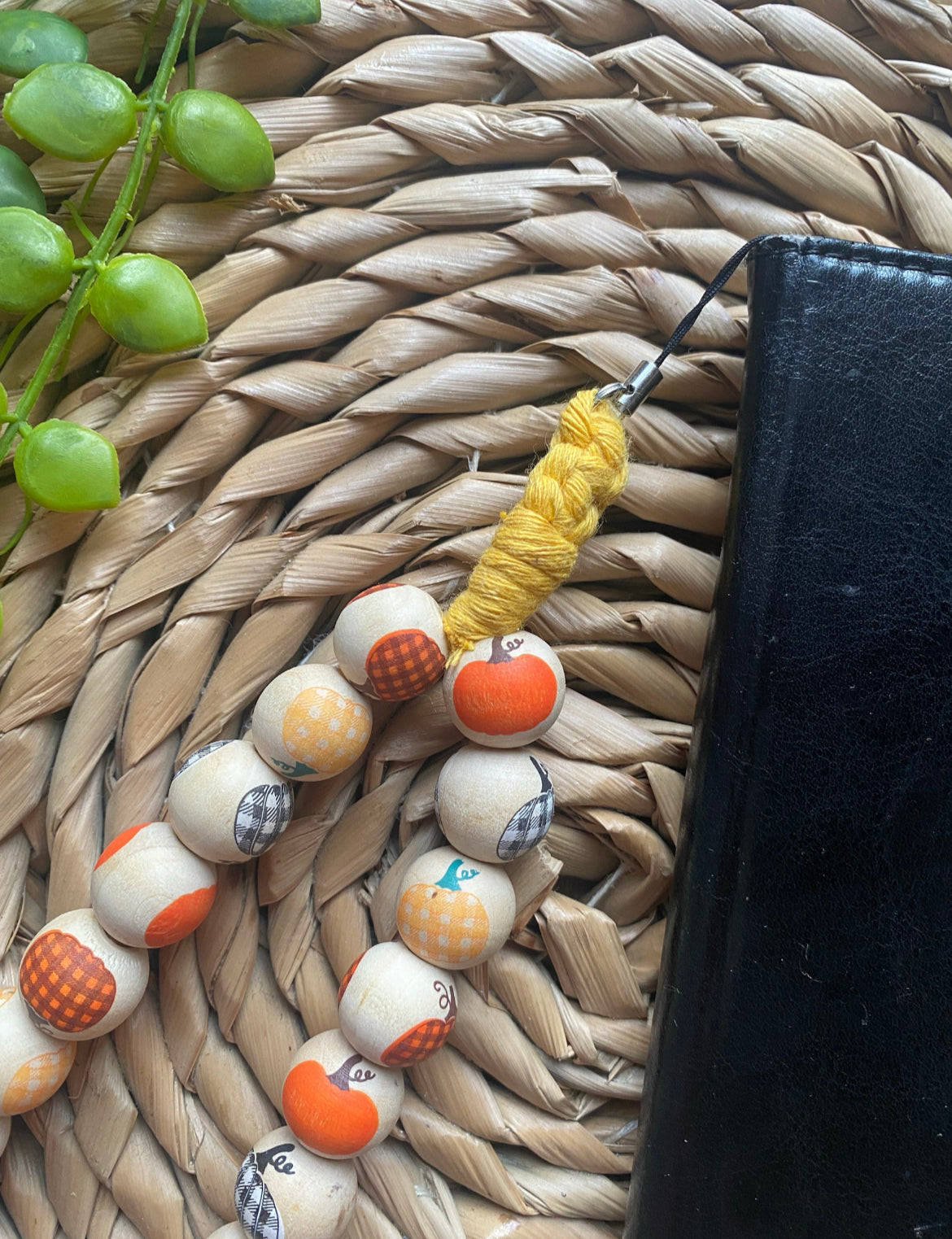 Close up of a handmade wristlet phone charm, made with pumpkin patterned wooden beads attached to a black wallet style phone case.