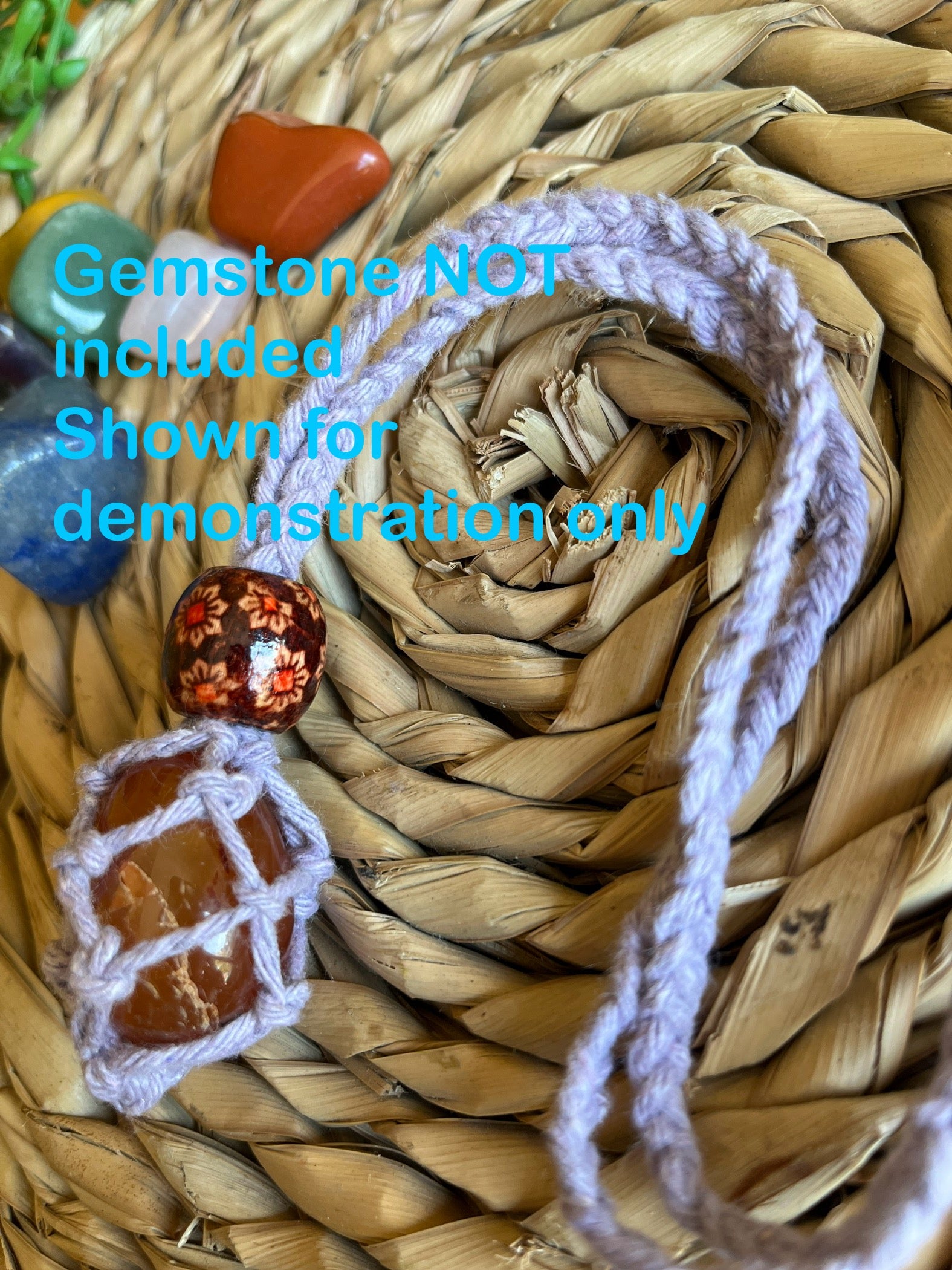 Macrame Gemstone Holder net pouch with orange gemstone inside, made with purple eco friendly recycled cotton and a Wooden bead. Blue text on the image explaining the gemstone is not included.