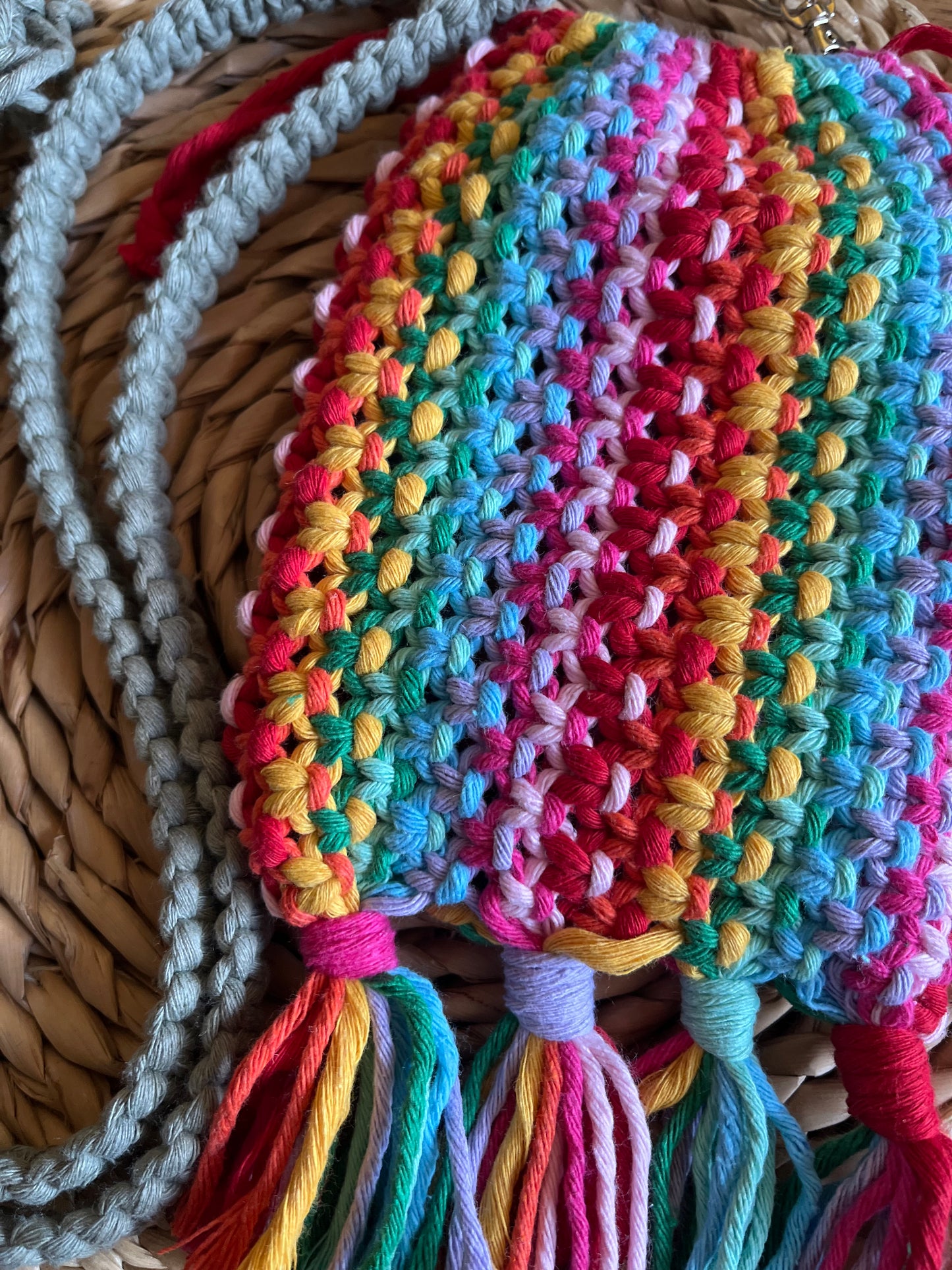 Close up of the intricate knots on a macrame crossbody bag, made with rainbow yarn, with tassels at the bottom.