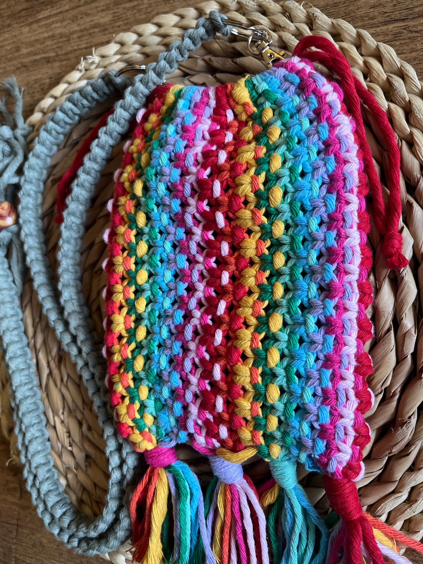 A handmade macrame crossbody bag, made with rainbow coloured yarn, laid on a round wicker mat.