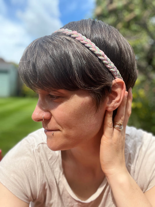 A person with short brown hair with her head turned sideways to the camera, wearing a multicoloured stretchy braided headband.