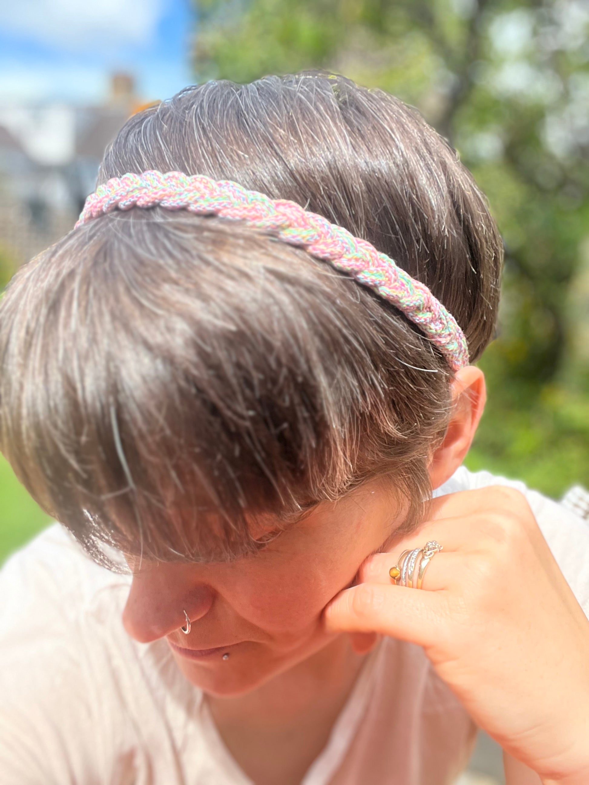 A person with short brown hair with her head turned away from the camera, wearing a multicoloured stretchy braided headband.