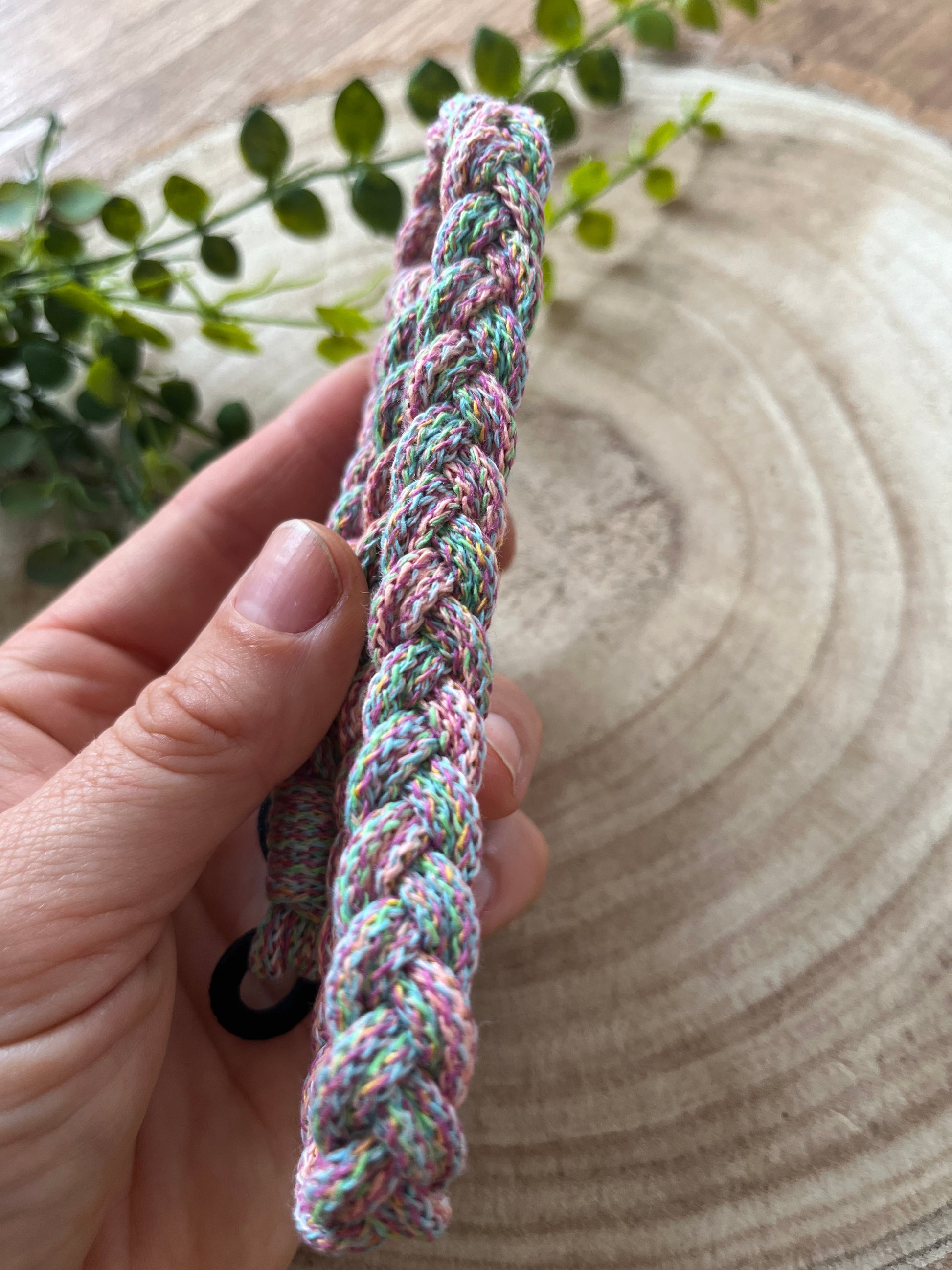 A hand holding a multicoloured stretchy braided headband.