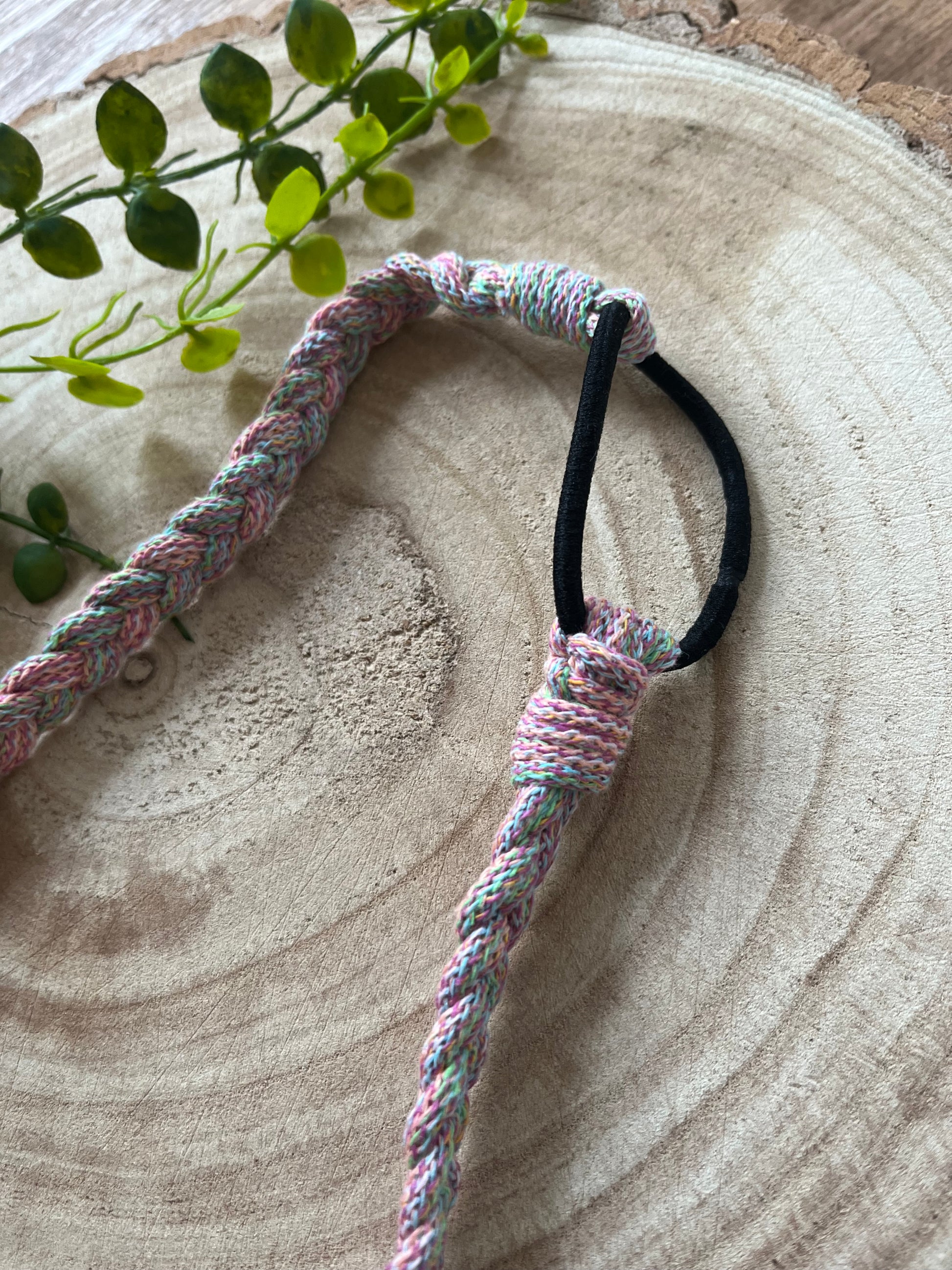 Close up of a multicoloured stretchy braided headband with black elastic finish.