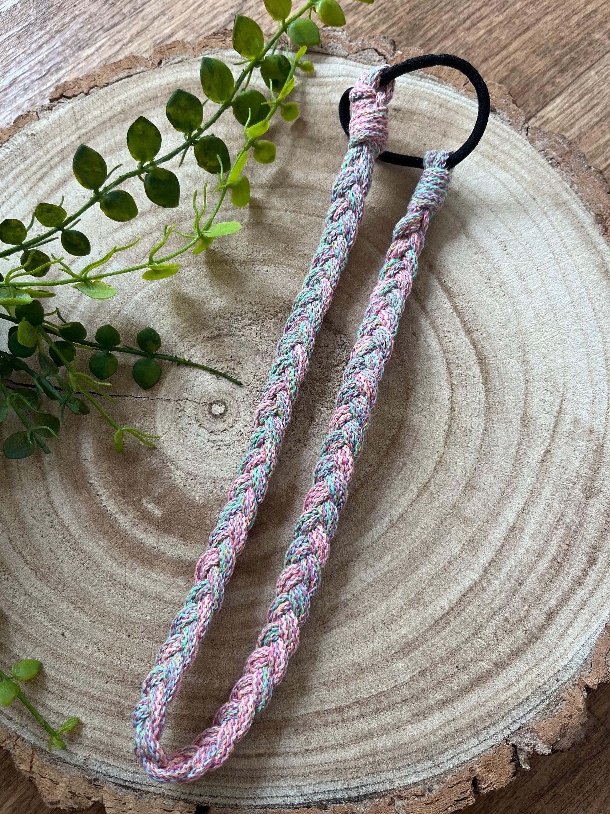 A handmade multicoloured stretchy braided headband on a wooden board.