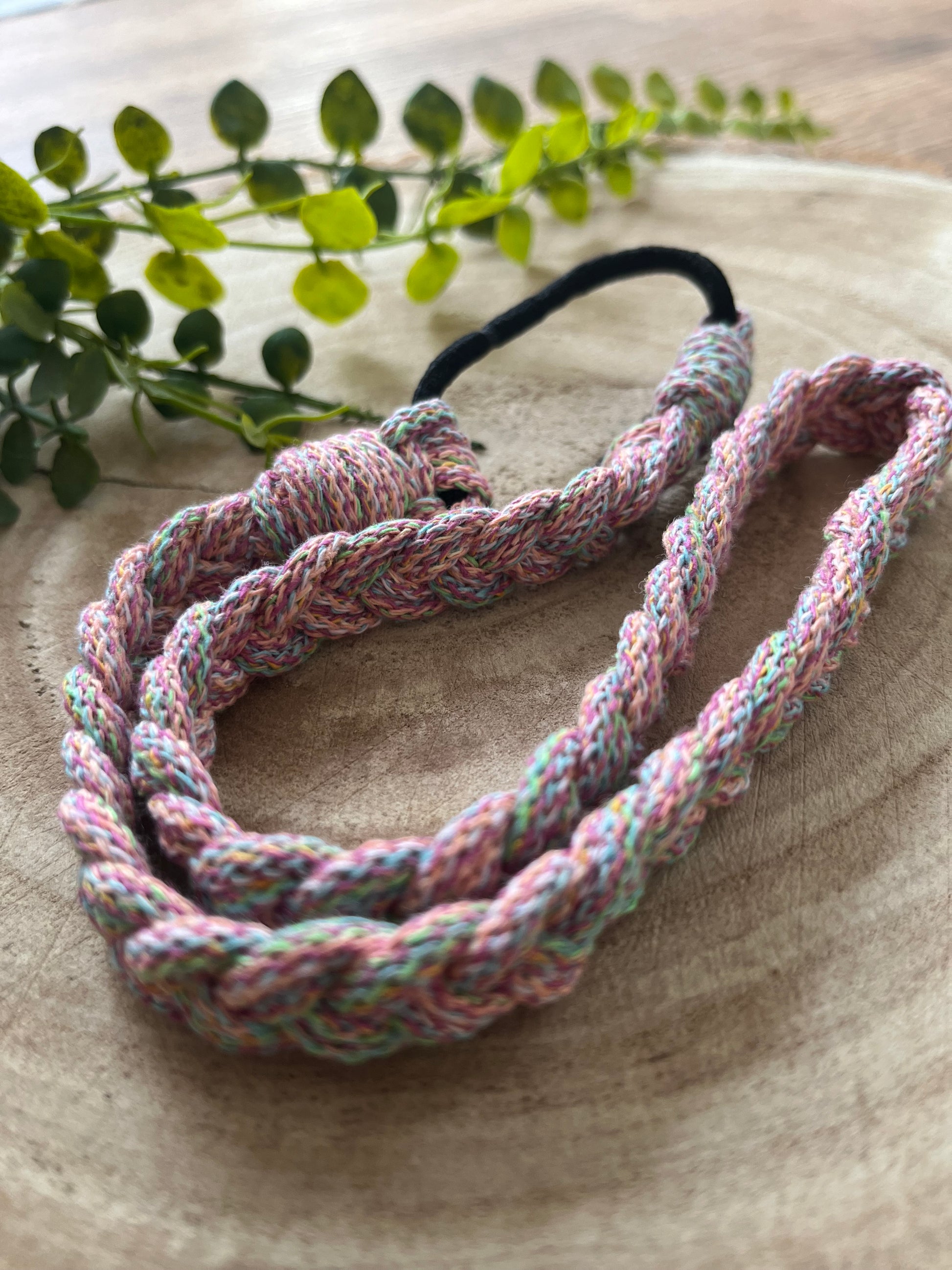 A handmade macrame multicoloured stretchy braided headband coiled on a wooden board.