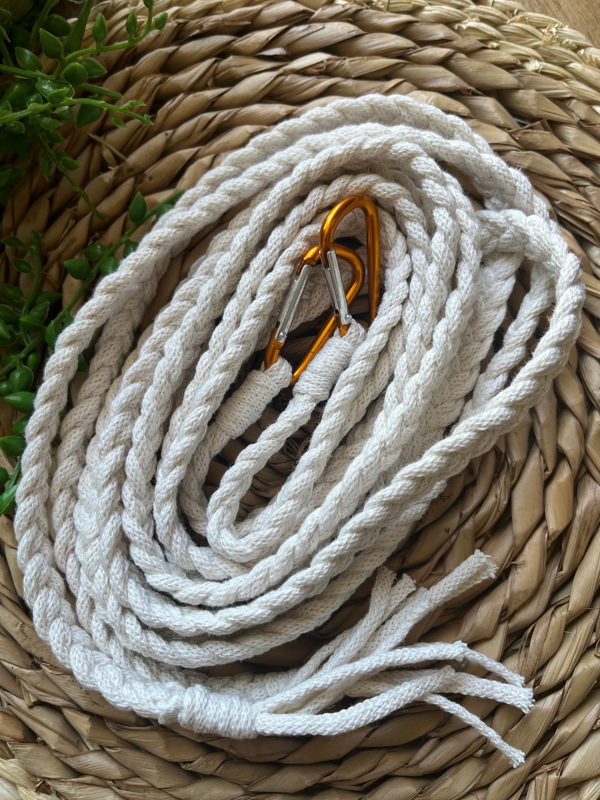 White braided macrame apron straps with orange carabiner clips, coiled neatly on top of a wicker placemat.