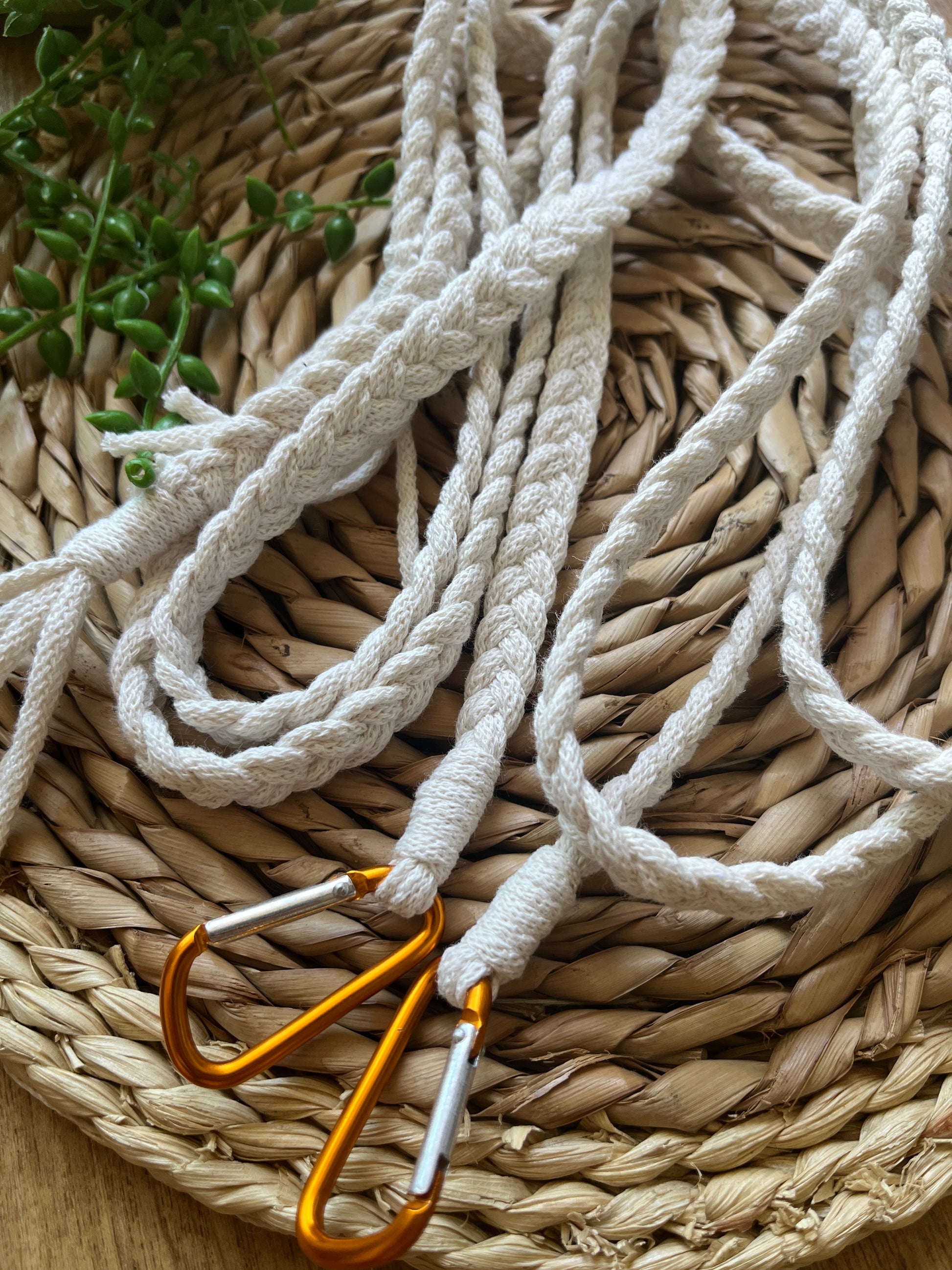 A close up of white braided apron straps with orange carabiner clips, coiled on top of a wicker placemat.