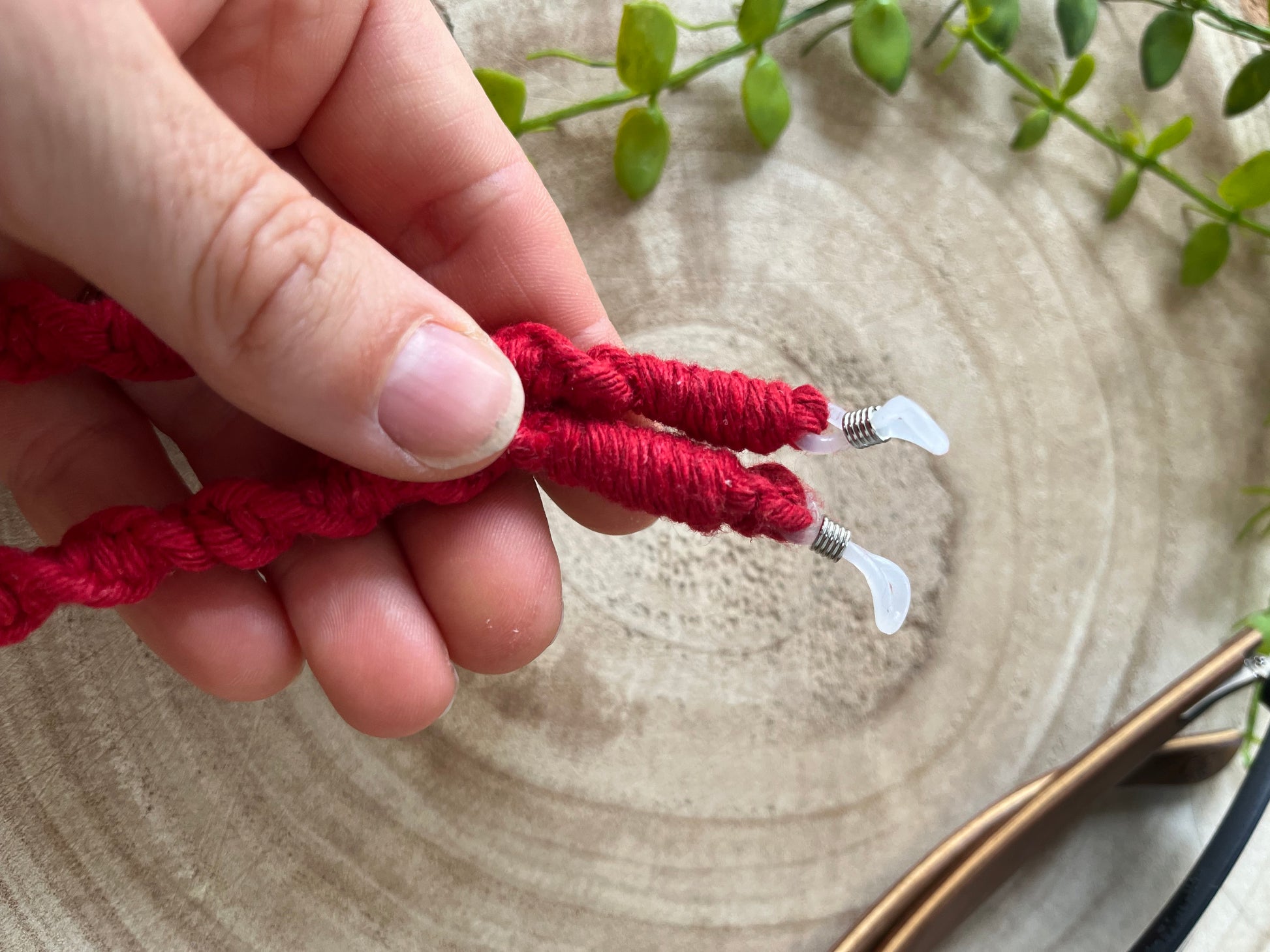 A hand holding a handmade macrame strap for glasses, made with red recycled cotton with clear loops on each end.