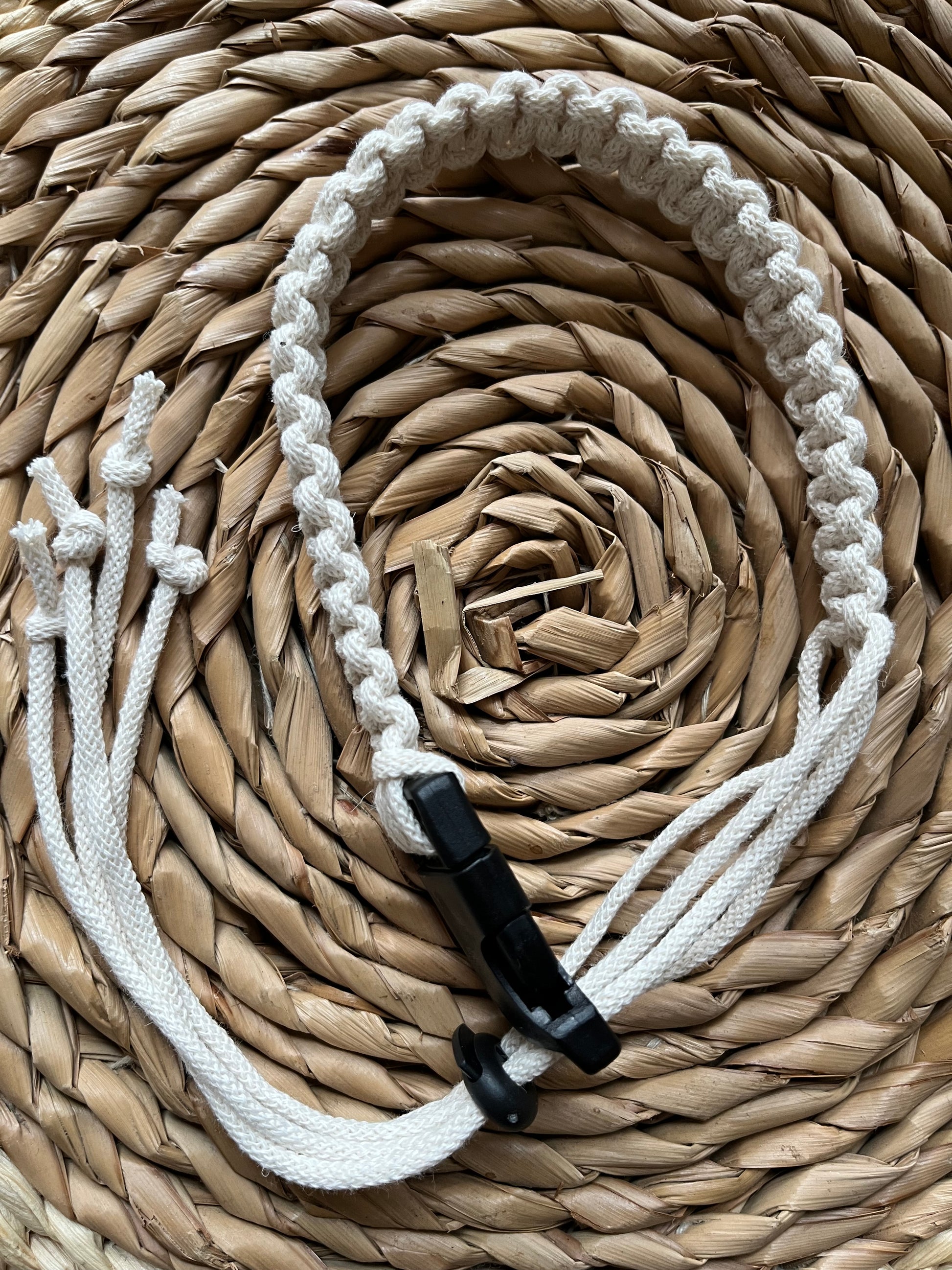 A handmade macrame knotted coffee cup holder strap, made with natural eco friendly recycled cotton, with a black buckle and toggle fastening.