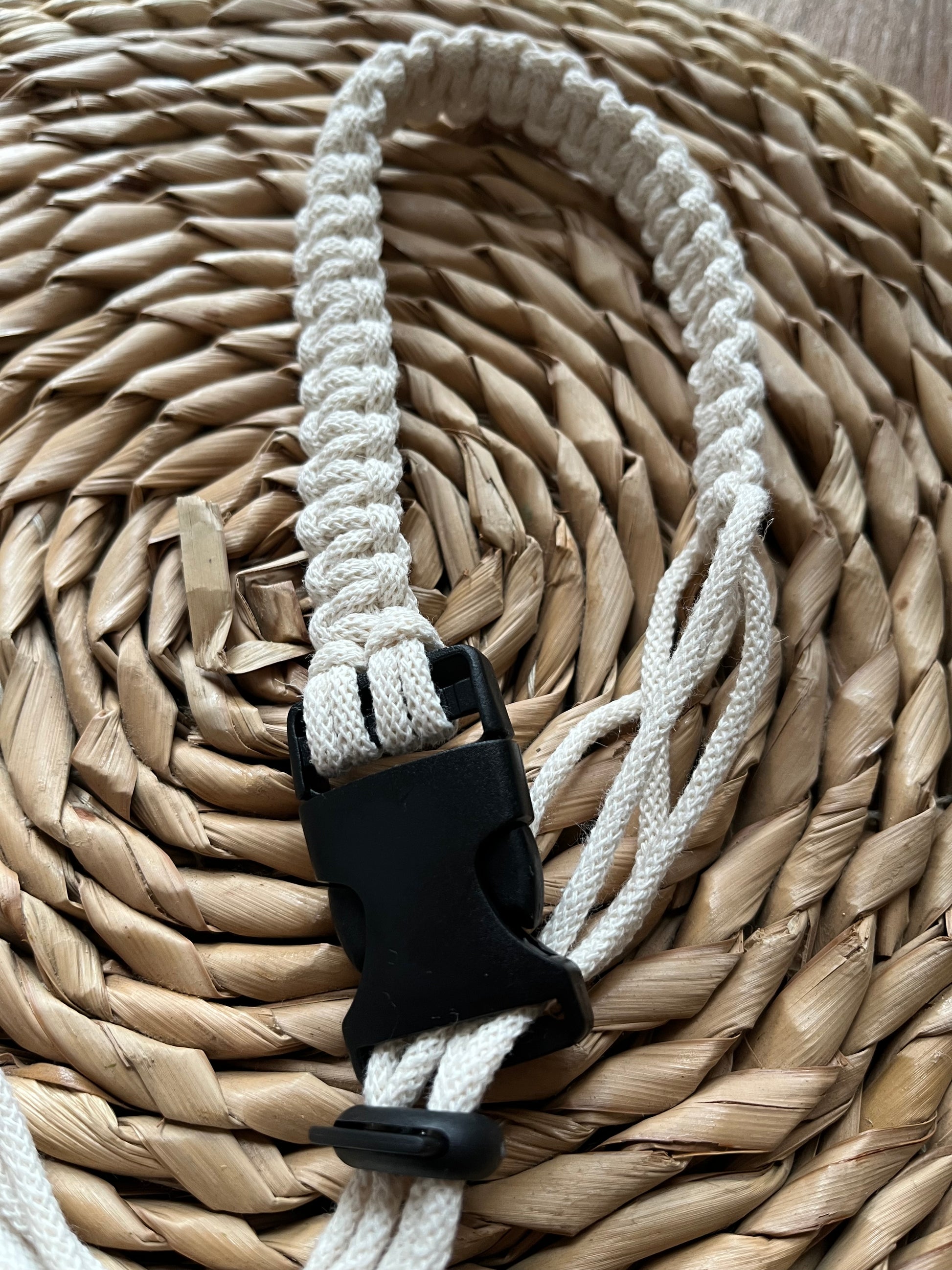 A handmade macrame knotted coffee cup holder strap, made with natural eco friendly recycled cotton, with a black buckle and toggle fastening.