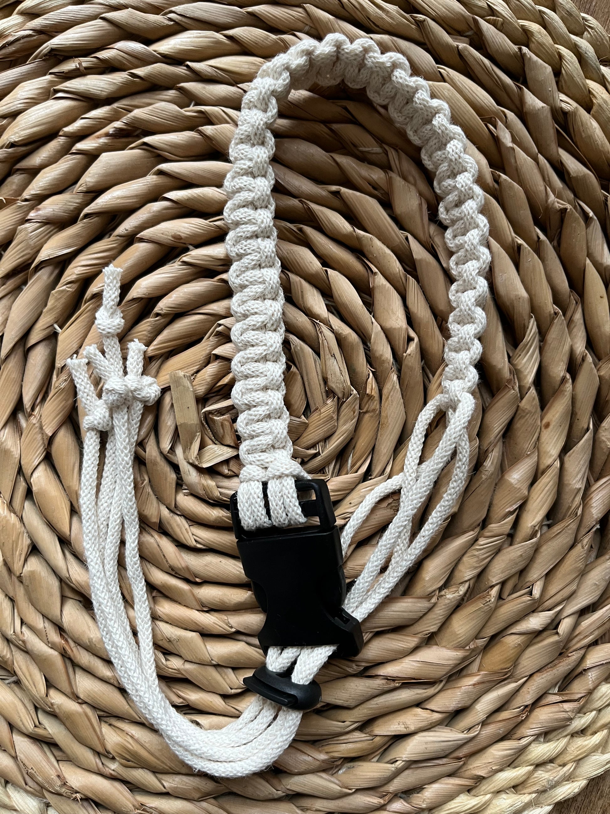 A handmade macrame knotted coffee cup holder strap, made with natural eco friendly recycled cotton, with a black buckle and toggle fastening.
