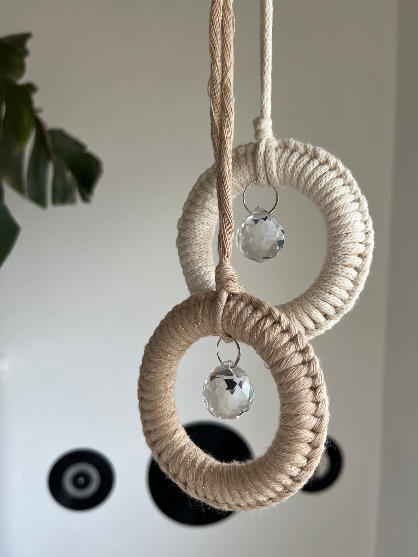 Two handmade macrame sun catchers, made with recycled cotton and small crystal prisms, hanging in front of a white wall.