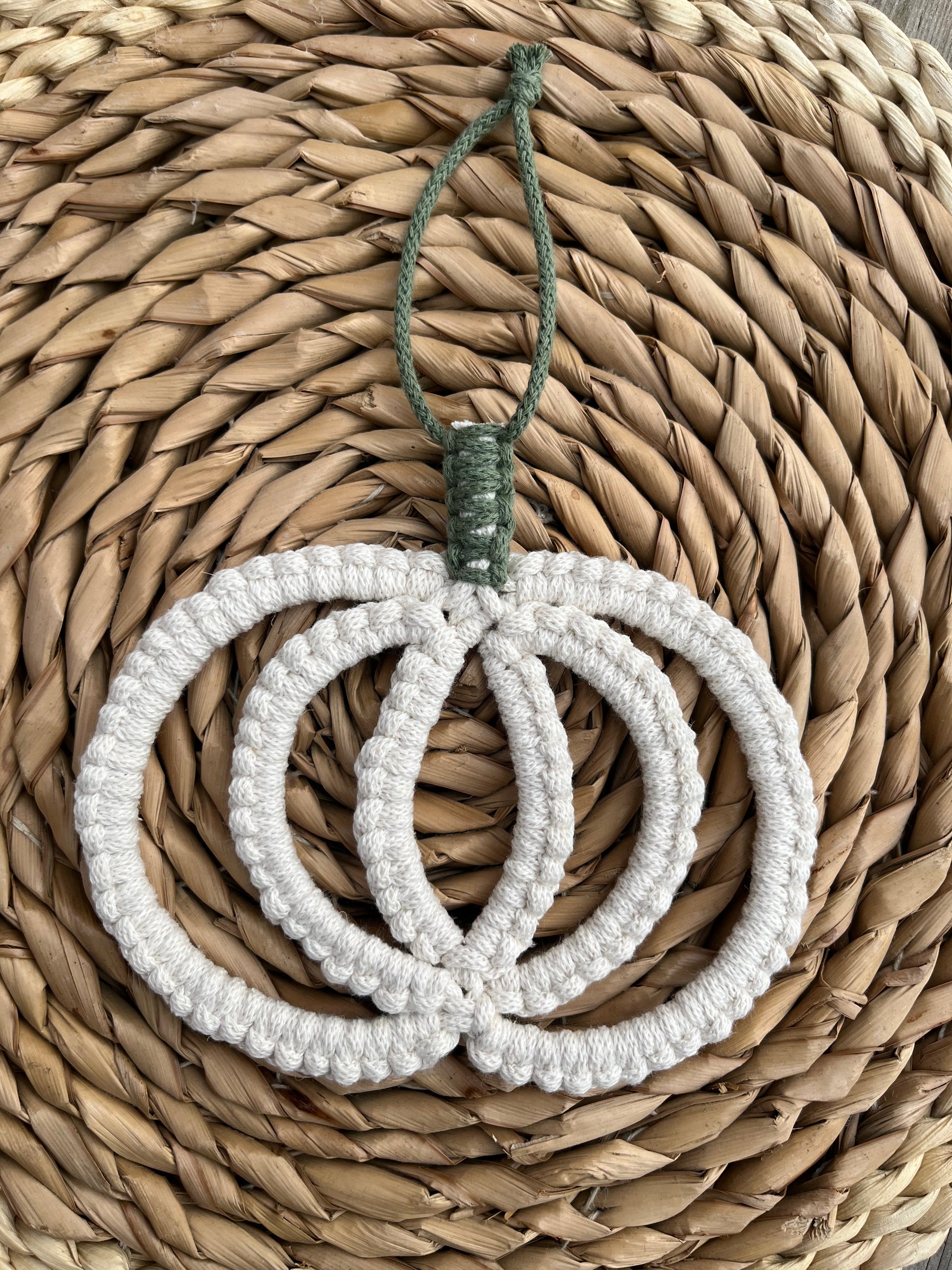 Pumpkin shaped macrame wall hanging decoration made with natural coloured recycled cotton yarn, placed on a wicker mat.