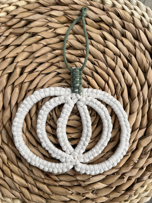 Pumpkin shaped macrame wall hanging decoration made with natural coloured recycled cotton yarn, placed on a wicker mat.