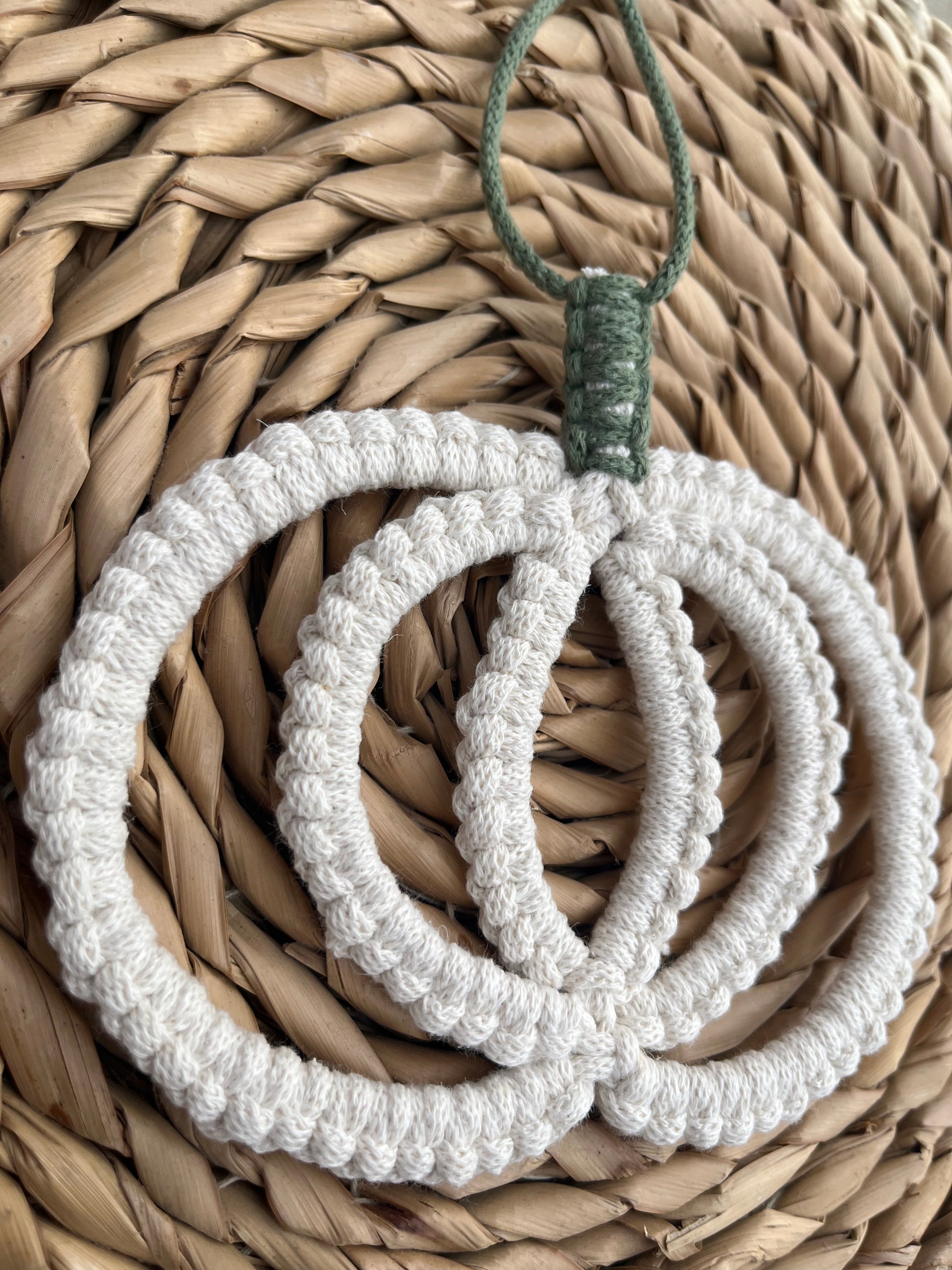 Close up of a pumpkin shaped macrame wall hanging decoration made with natural coloured recycled cotton yarn, placed on a wicker mat.