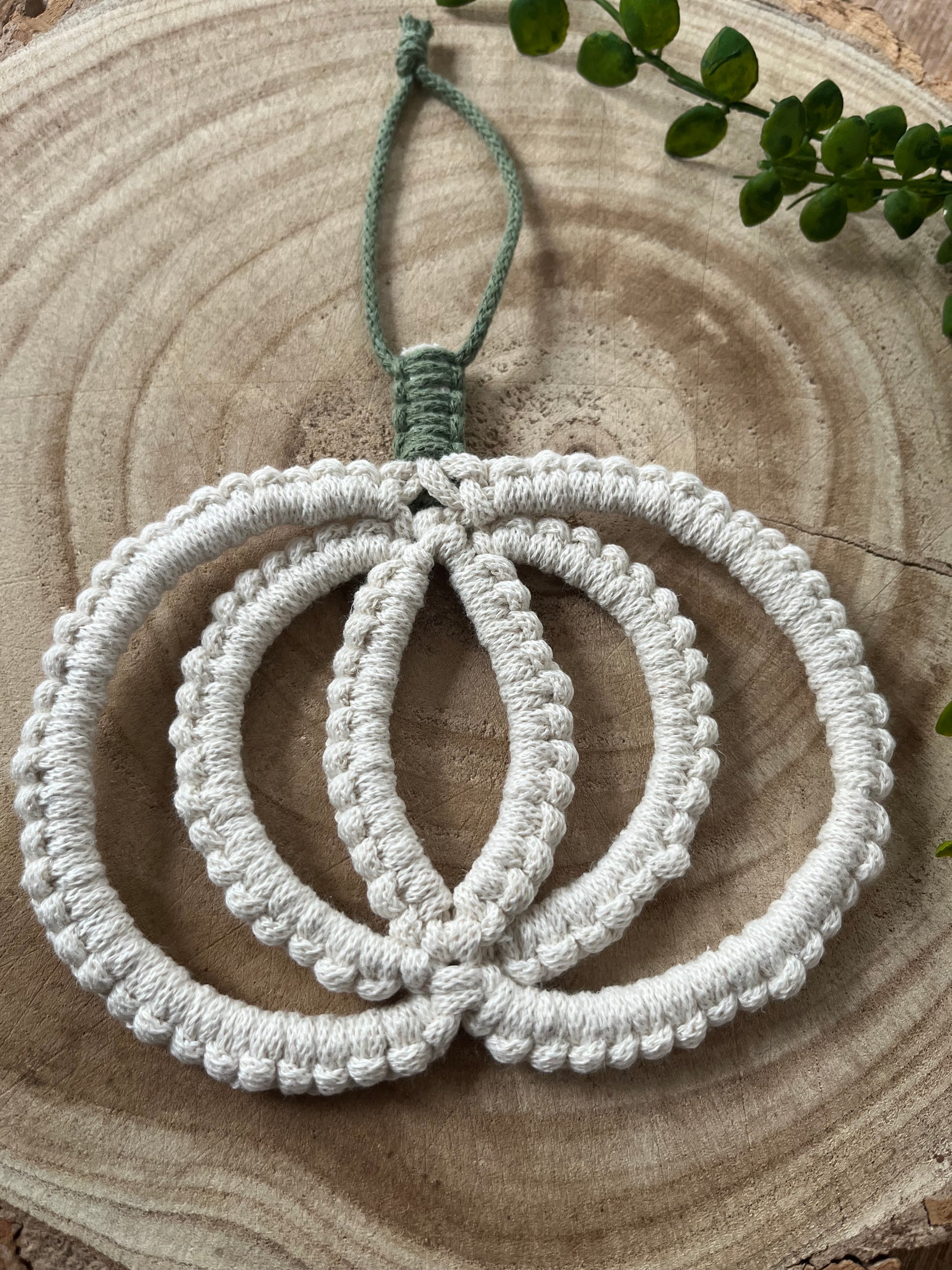 Pumpkin shaped macrame wall hanging decoration made with natural coloured recycled cotton yarn, on a wooden board.