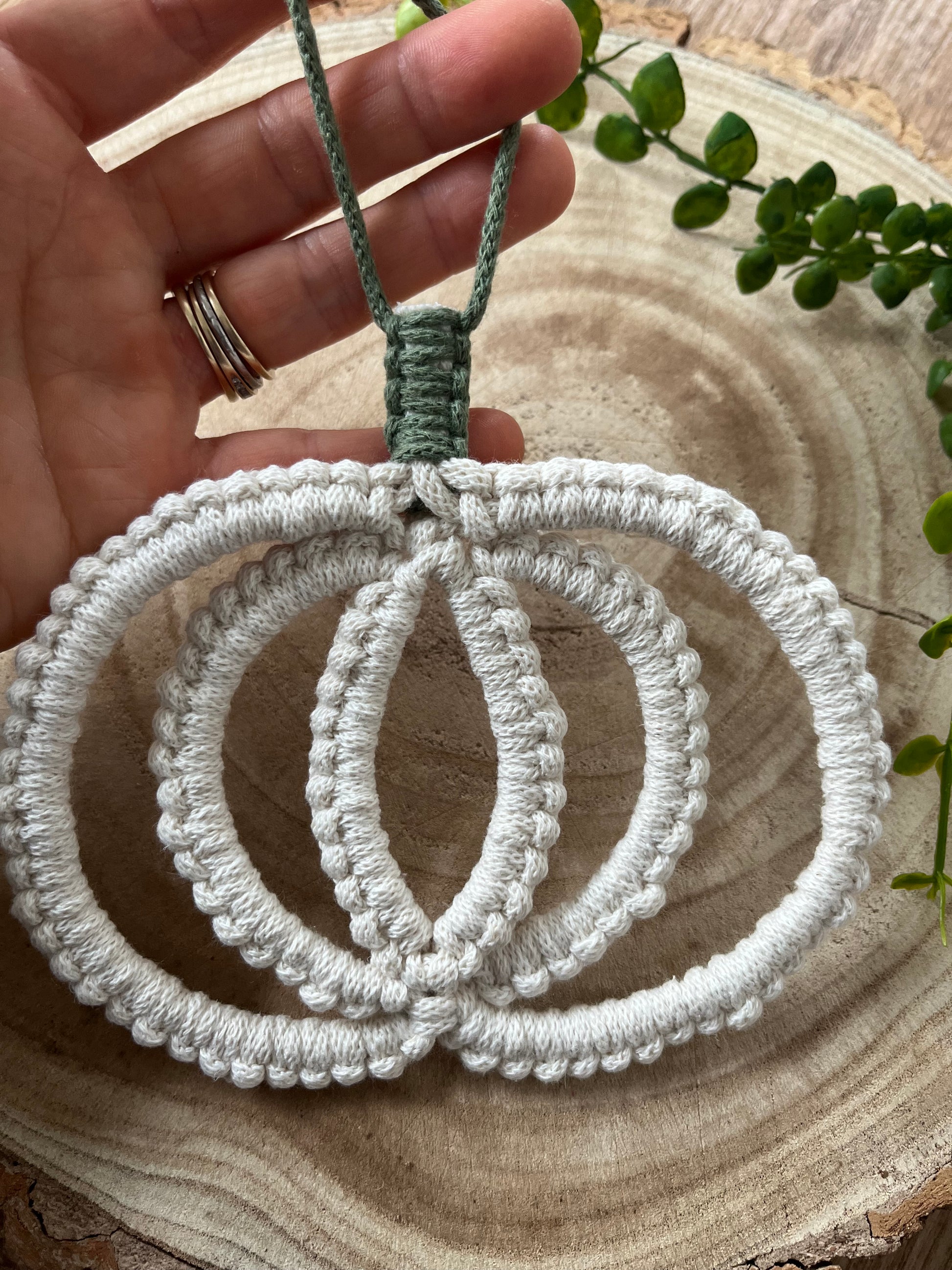 A hand holding a pumpkin shaped macrame wall hanging decoration made with natural coloured recycled cotton yarn.