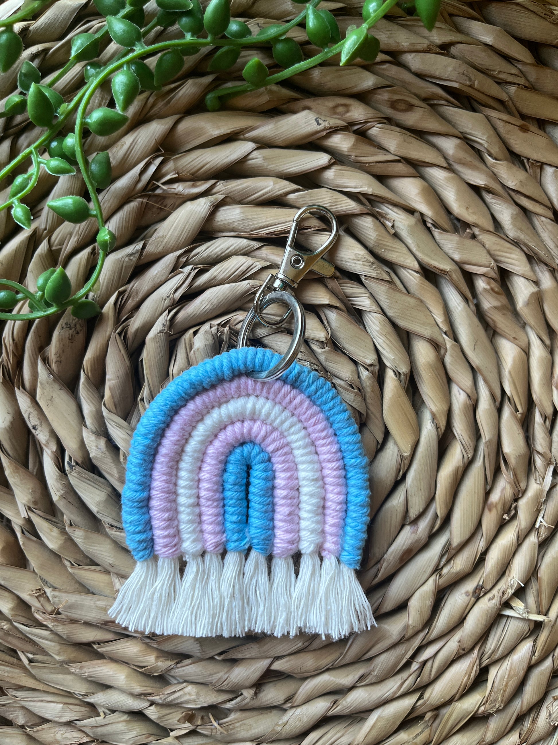 Handmade macrame rainbow keyring, made with blue, pink and white yarns to represent the colours of the trans pride flag. The keyring has a silver split ring and lobster clasp at the top.