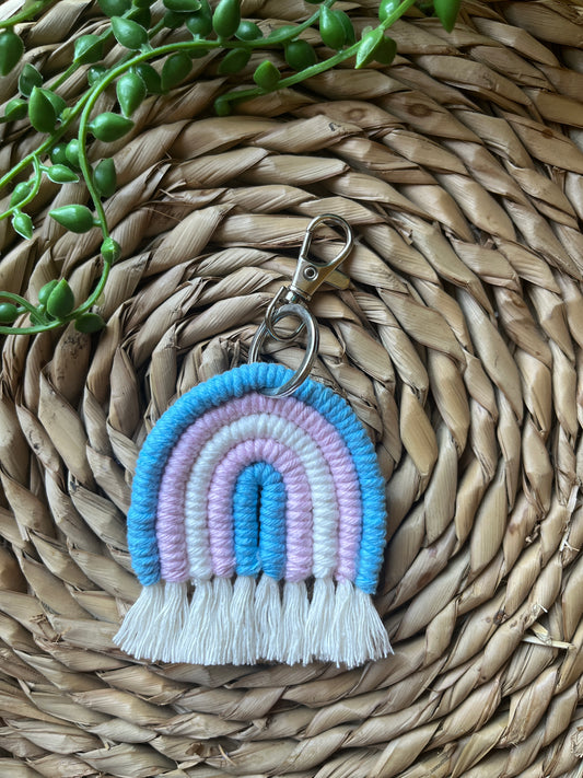 Handmade macrame rainbow keyring, made with blue, pink and white yarns to represent the colours of the trans pride flag. The keyring has a silver split ring and lobster clasp at the top.