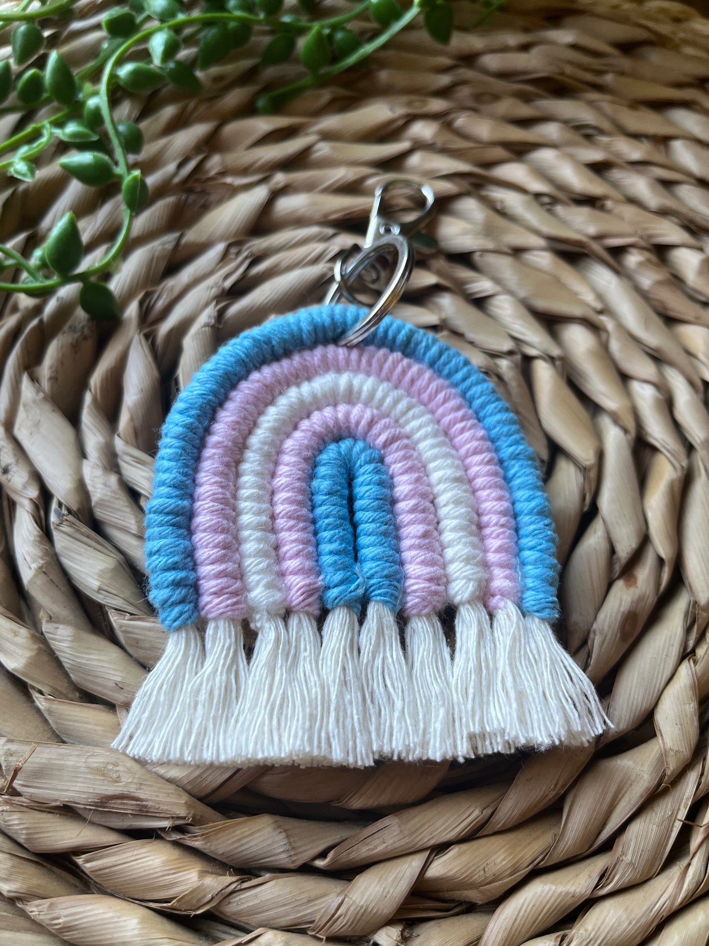 Handmade macrame rainbow keyring, made with blue, pink and white yarns to represent the colours of the trans pride flag. The keyring has a silver split ring and lobster clasp at the top.