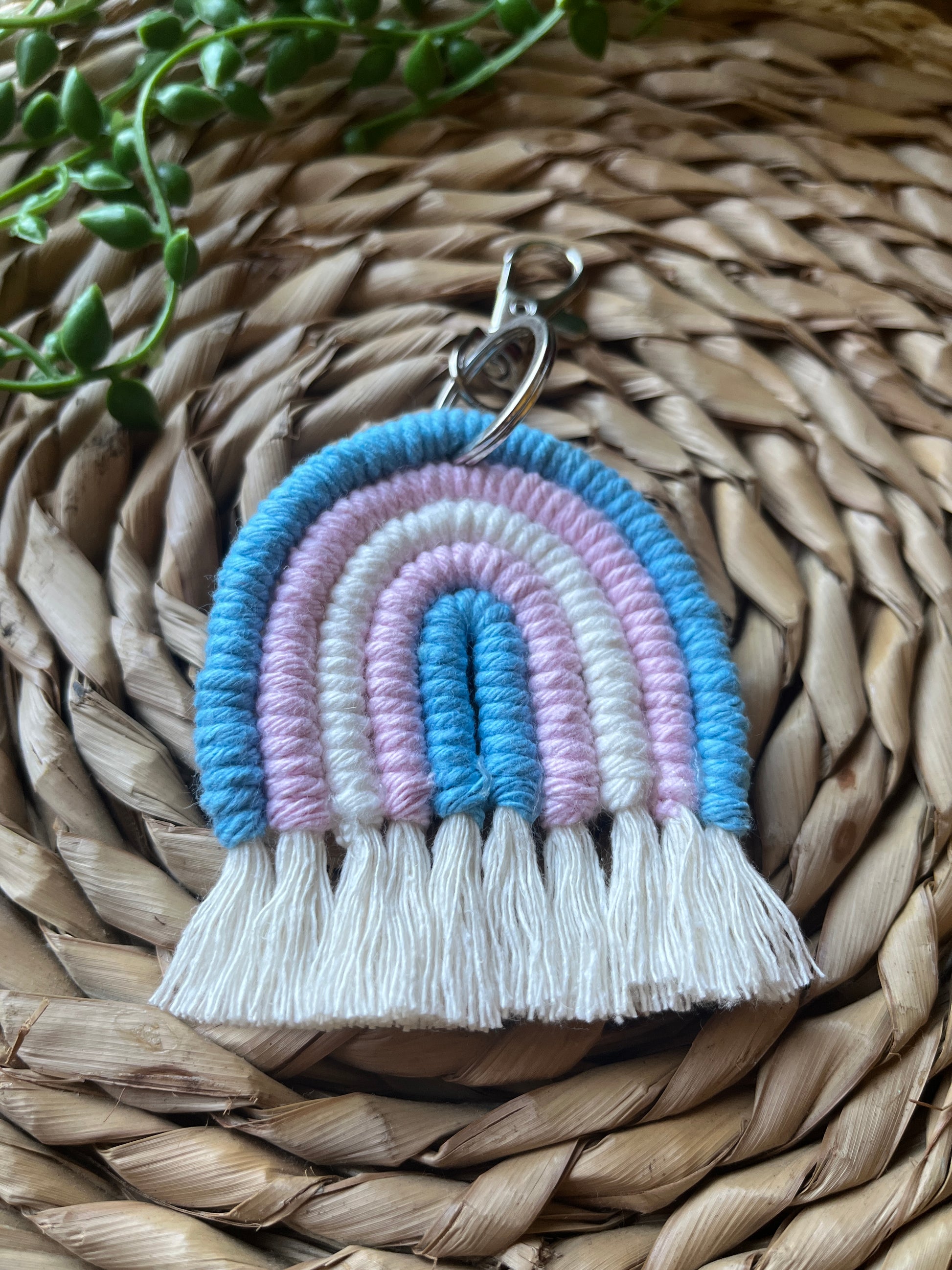 Handmade macrame rainbow keyring, made with blue, pink and white yarns to represent the colours of the trans pride flag. The keyring has a silver split ring and lobster clasp at the top.