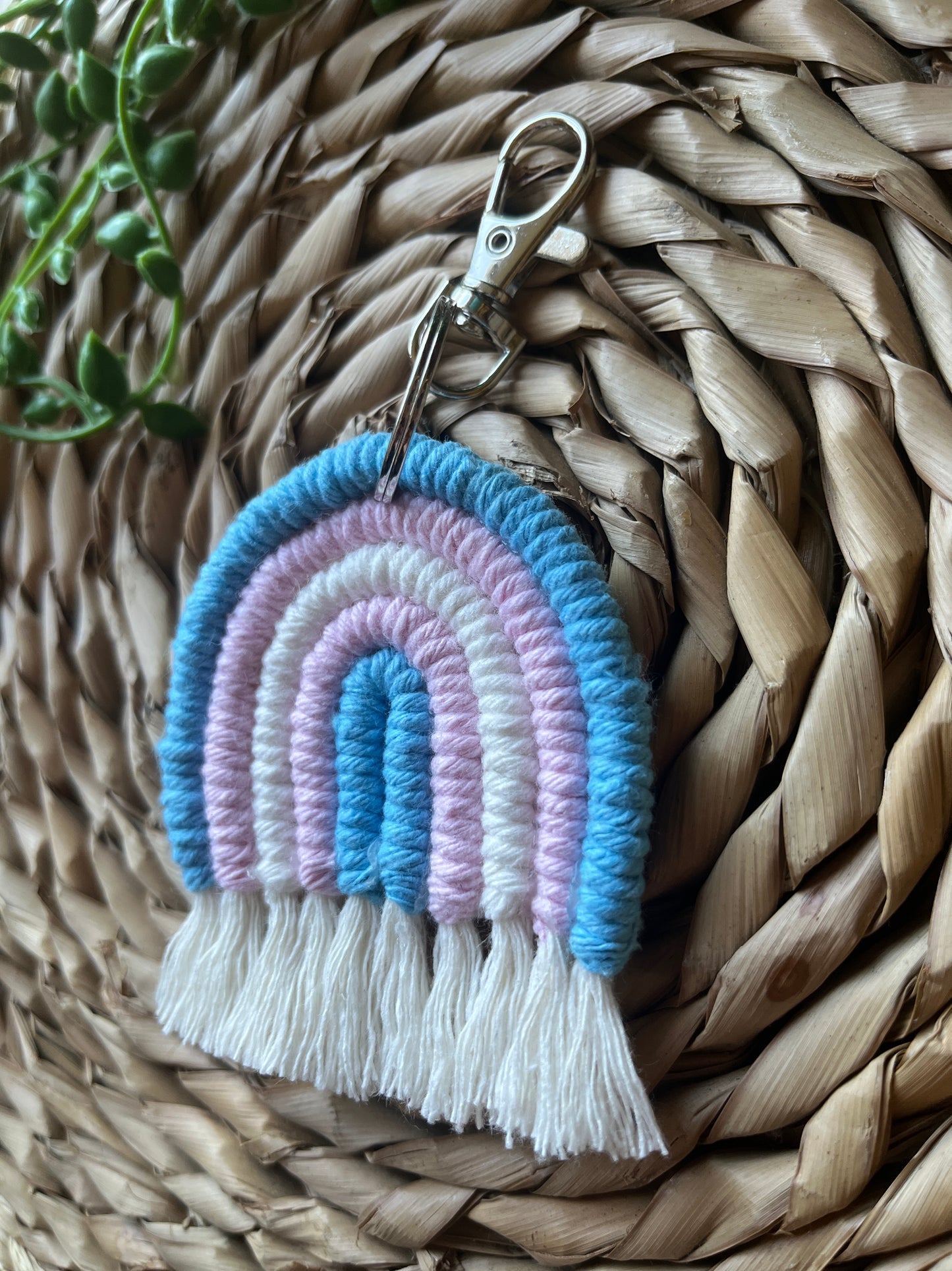 Handmade macrame rainbow keyring, made with blue, pink and white yarns to represent the colours of the trans pride flag. The keyring has a silver split ring and lobster clasp at the top.