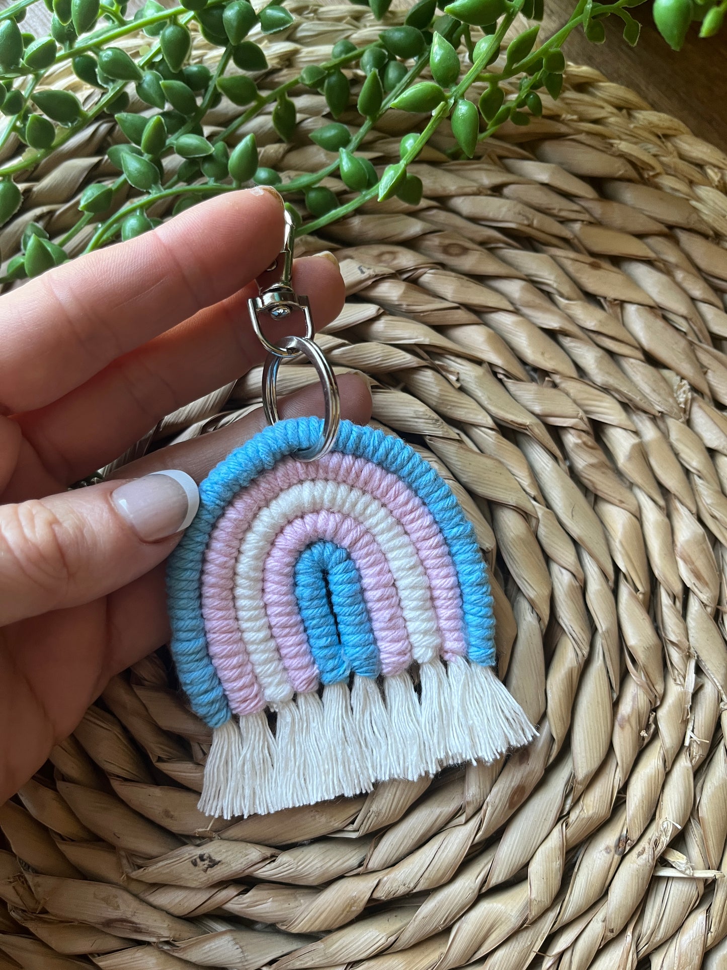 Handmade macrame rainbow keyring, made with blue, pink and white yarns to represent the colours of the trans pride flag. The keyring has a silver split ring and lobster clasp at the top.