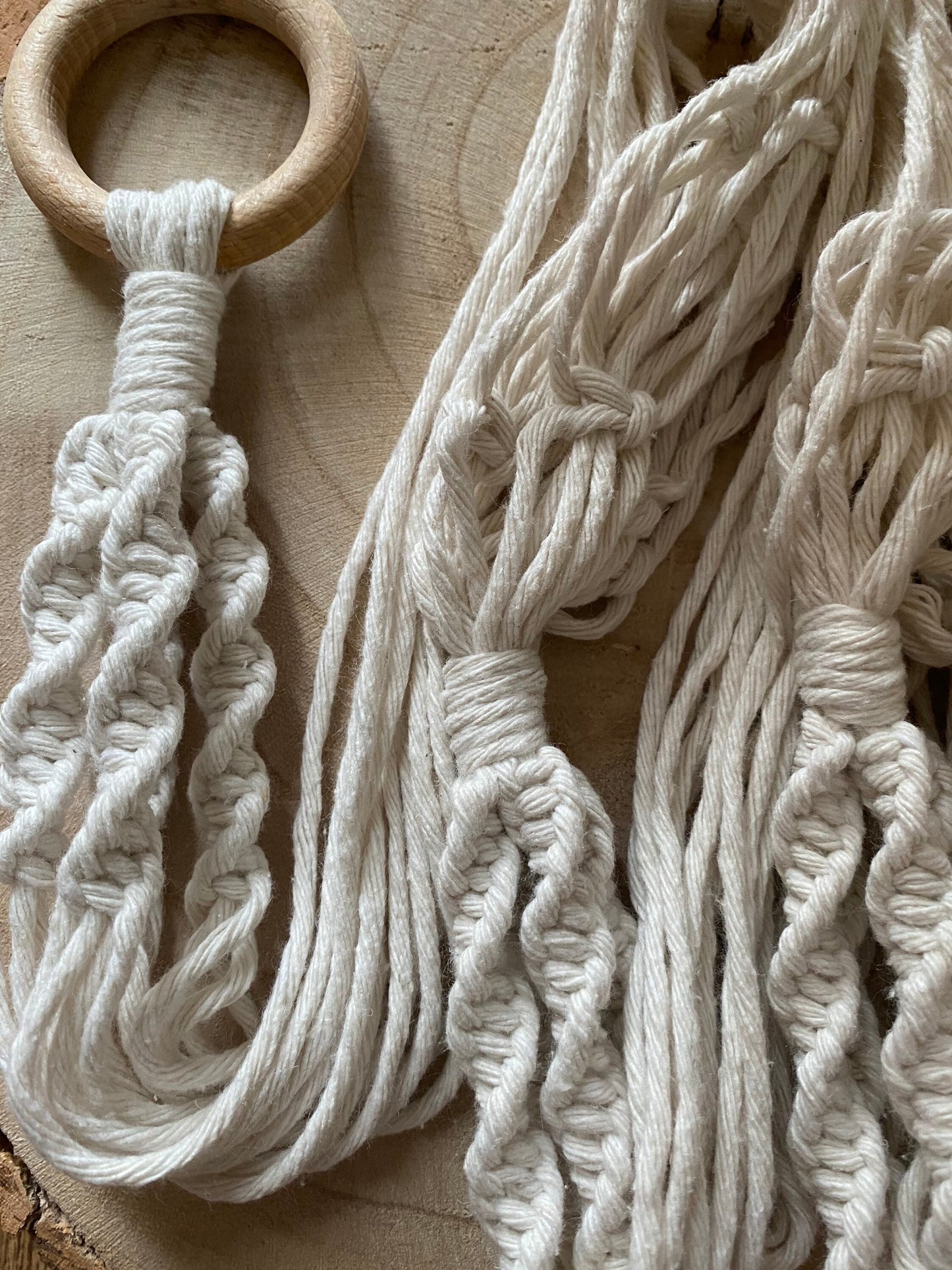 Close up image of the intricate knot pattern on a macrame plant hanger, made with natural coloured cotton yarn and a wooden ring.