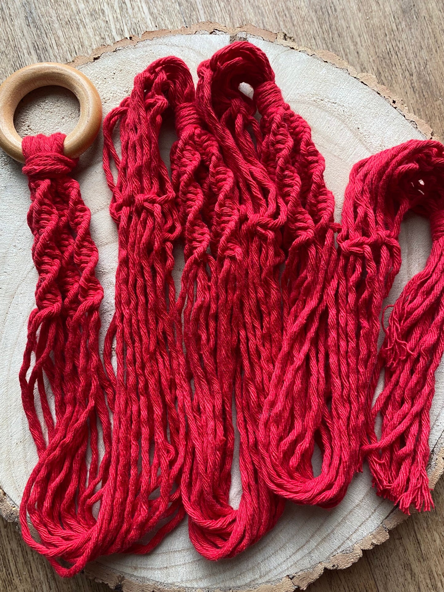 A large red macrame plant hanger with twisted knot pattern and wooden ring, is folded neatly on a round wooden surface.