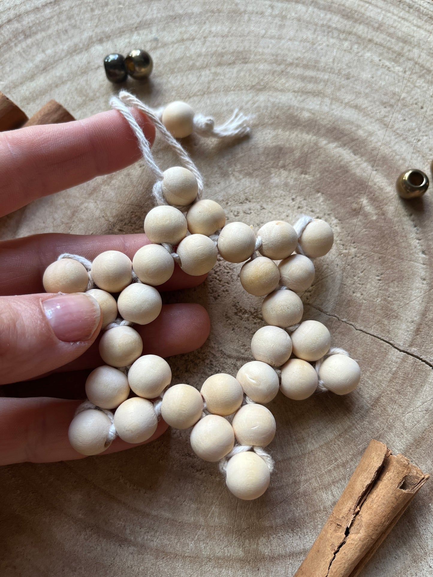 A hand holding a star-shaped hanging decoration, made of small wooden beads and natural yarn.