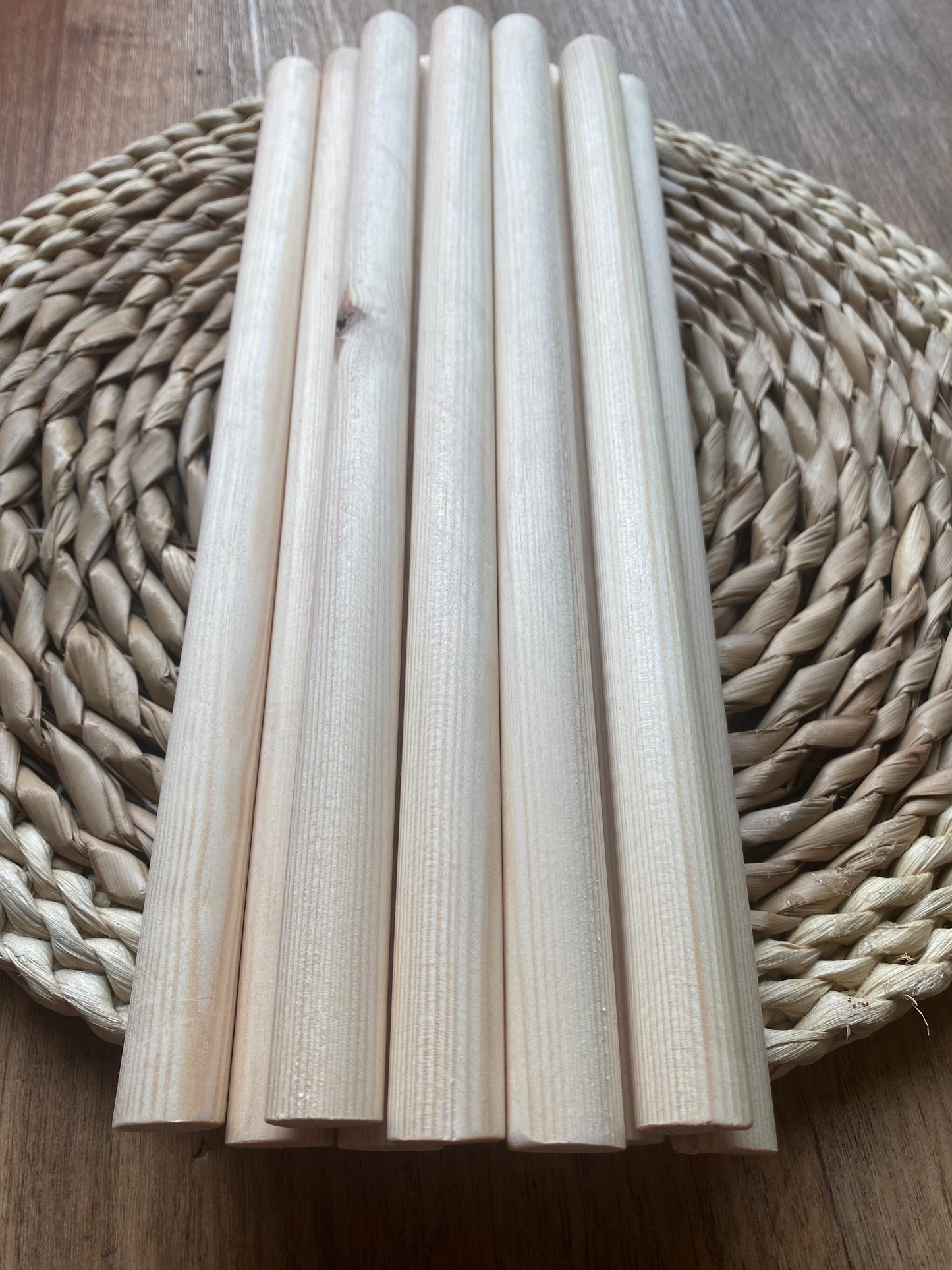 A stack of natural pine wooden dowels for macramé and crafts, laid across a round wicker mat.