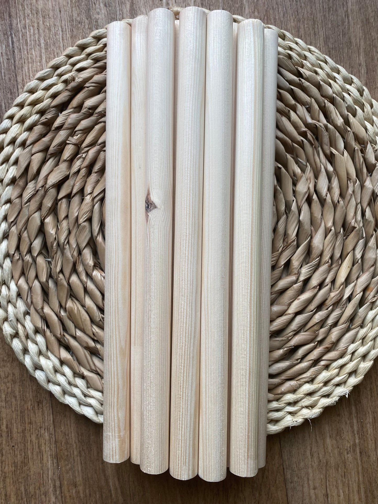 A pile of natural pine wooden dowels for macramé and crafts laid across a round wicker mat.