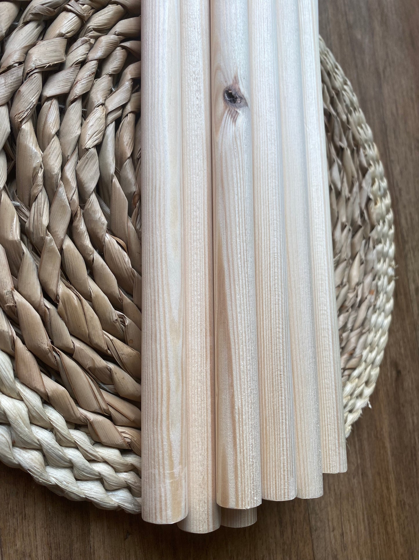 Close up of a pile of natural pine wooden dowels for macramé and crafts laid across a round wicker mat.