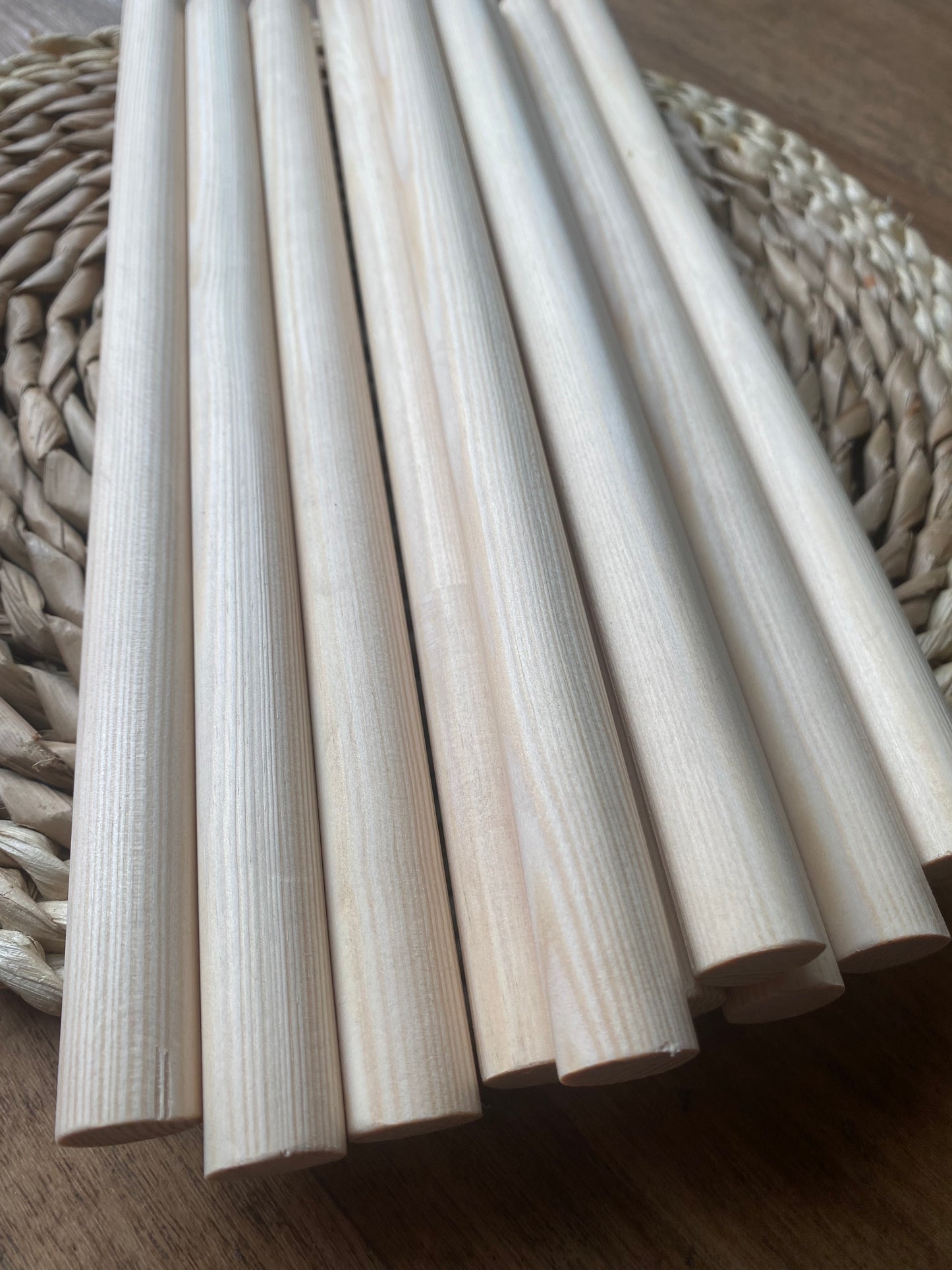 Close up of a pile of natural pine wooden dowels for macramé and crafts laid across a round wicker mat.