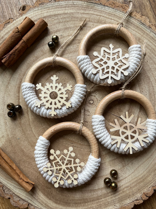 Decorative wooden ornaments, made on wooden rings with natural yarn and finished with wooden snowflake designs, displayed on a rustic wooden surface.