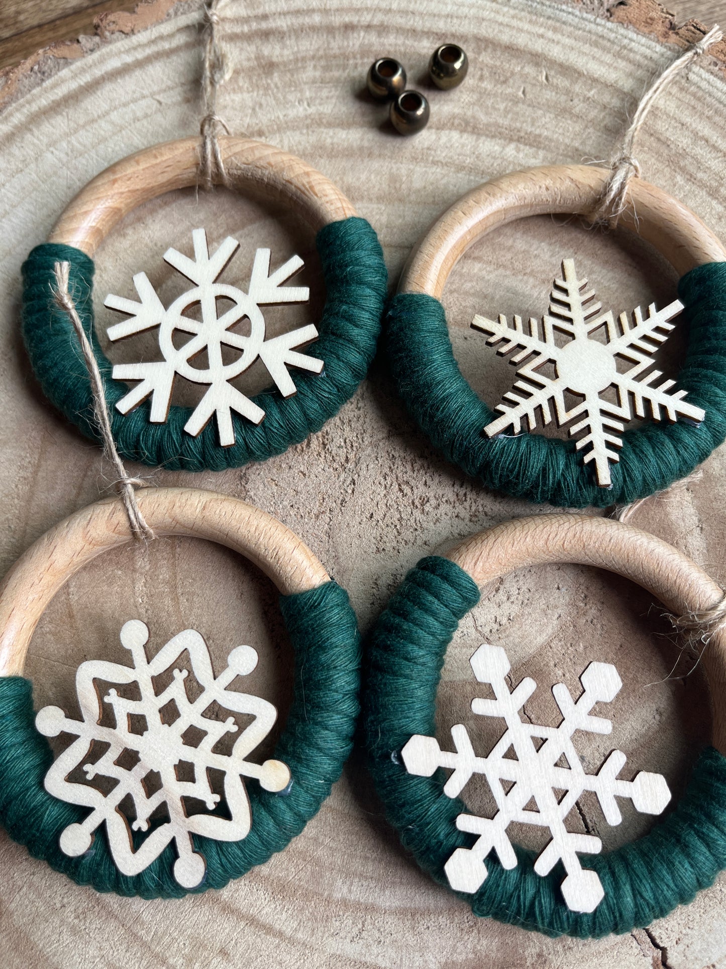 Decorative wooden ornaments, made on wooden rings with pine green cotton yarn and finished with wooden snowflake designs, displayed on a rustic wooden surface.