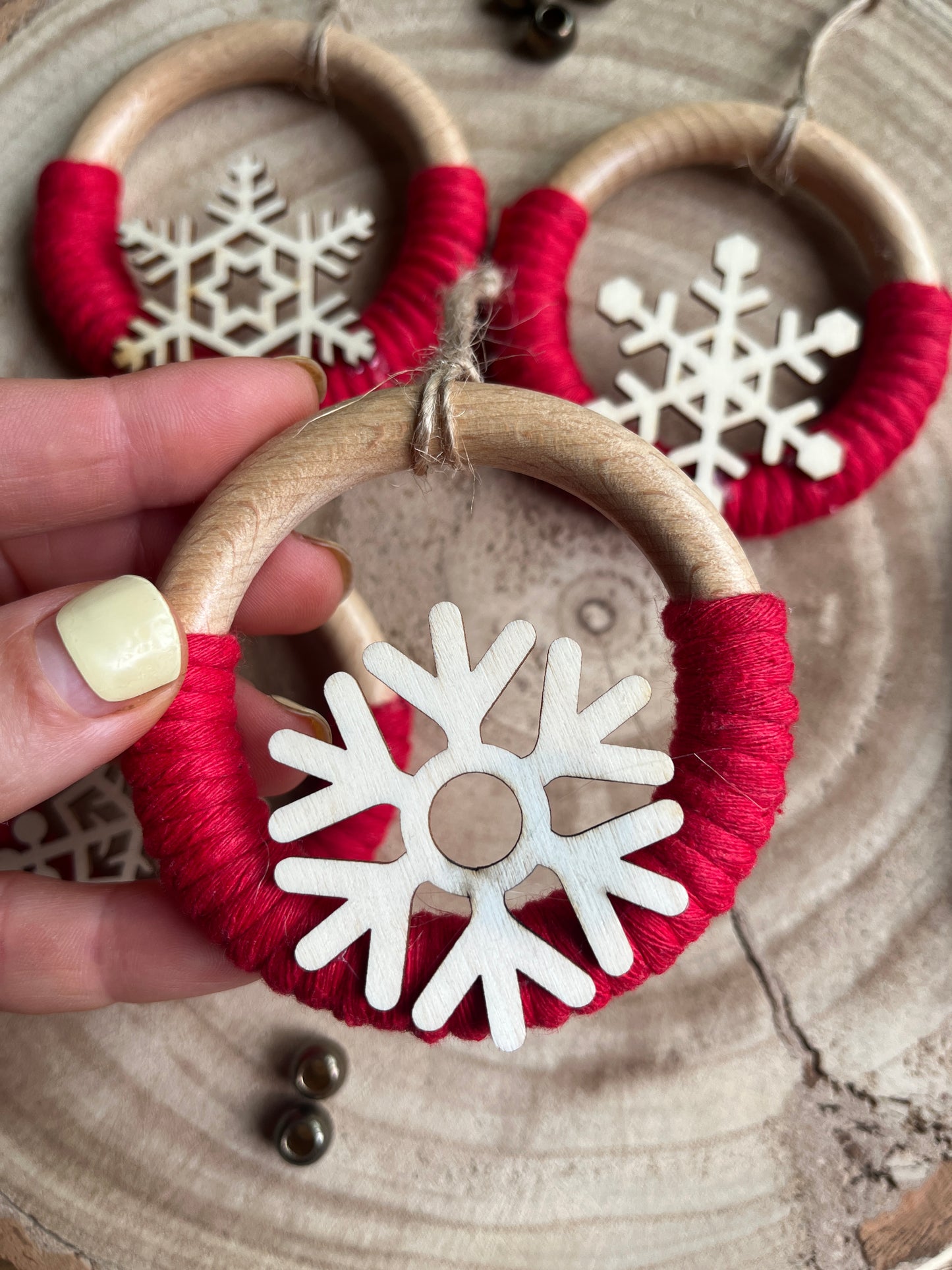 A hand holding a decorative wooden ornament, made on a wooden ring with red yarn and finished with a wooden snowflake design.