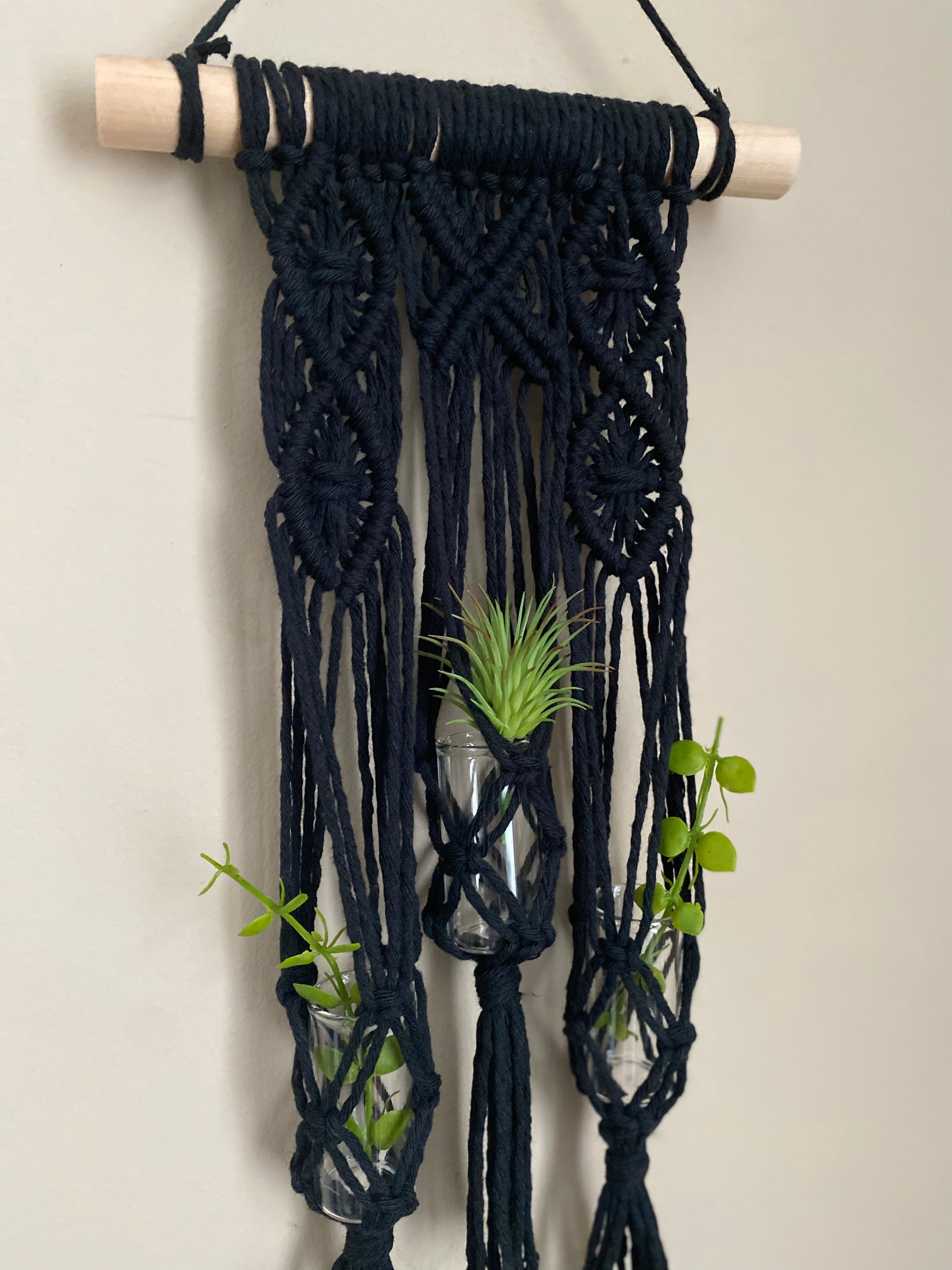 Close up showing intricate knot pattern on macrame wall hanger houseplant propagation station in black yarn on a wooden dowel.