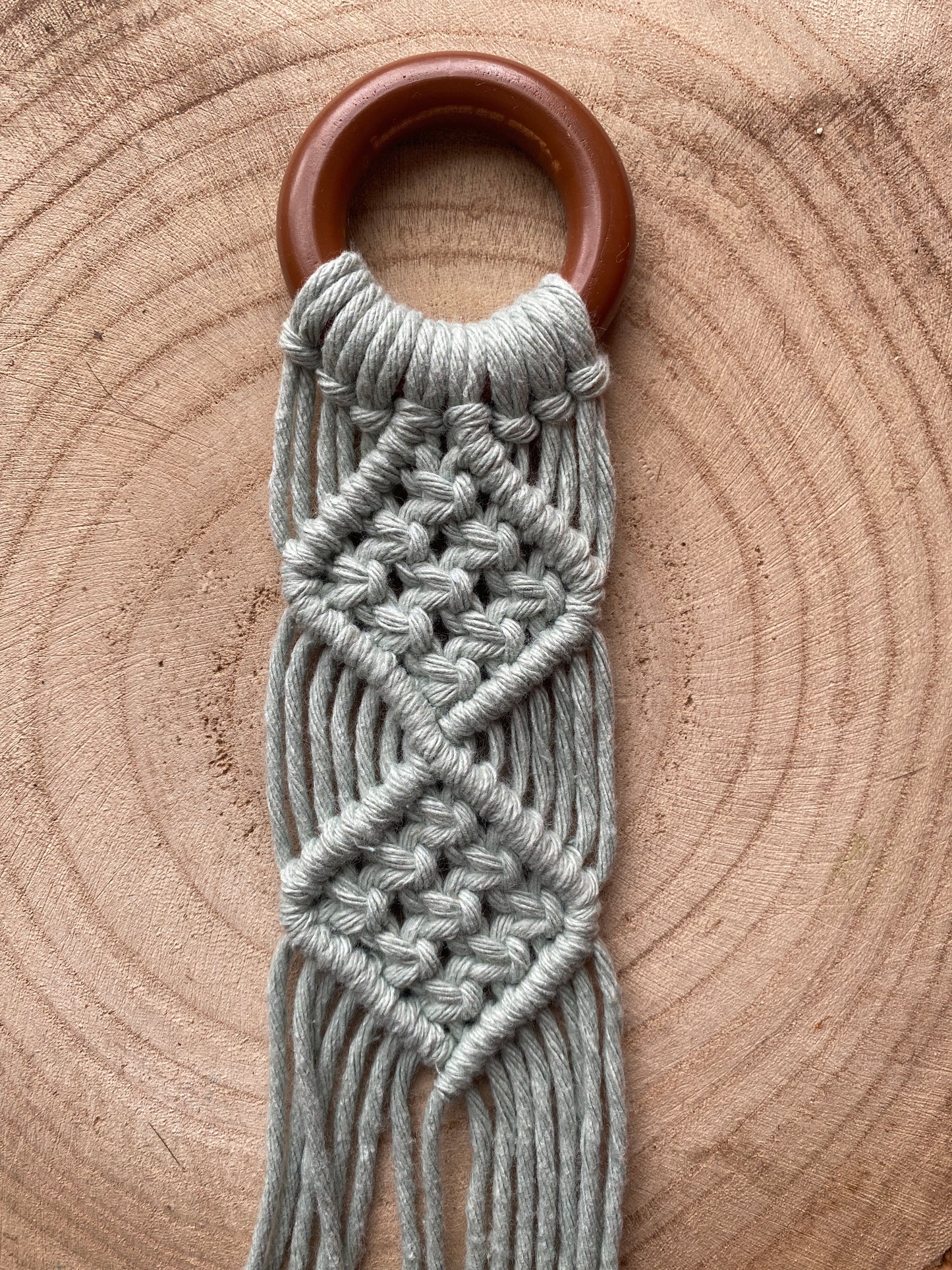Close up image of the intricate knot pattern on the top section of a macrame instrument wall hanger, made with pastel green yarn on a dark wooden ring.