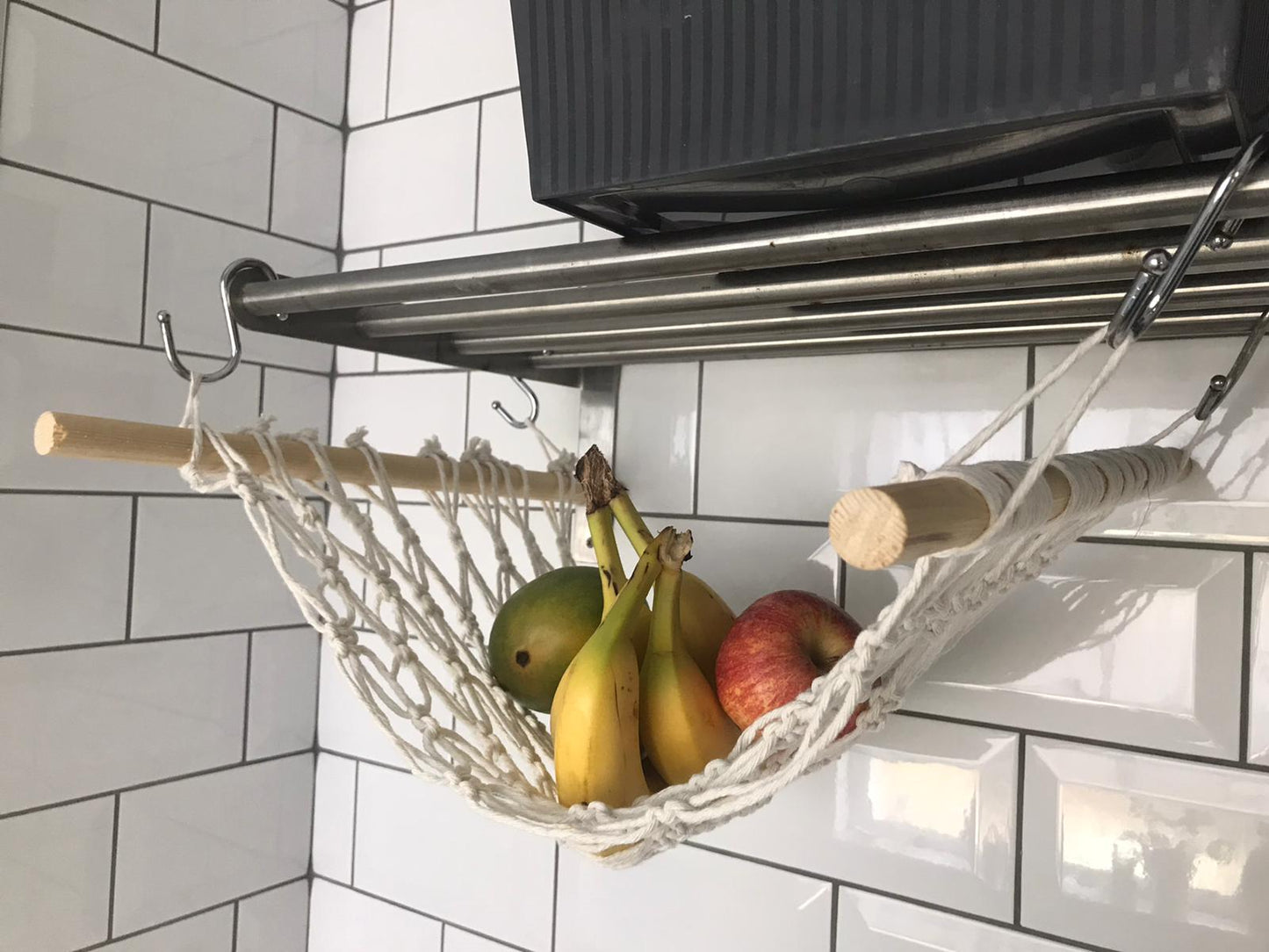 Bananas and apples hang in a macrame hammock made with natural recycled cotton and wooden dowels, underneath a metal shelf from metal S hooks.