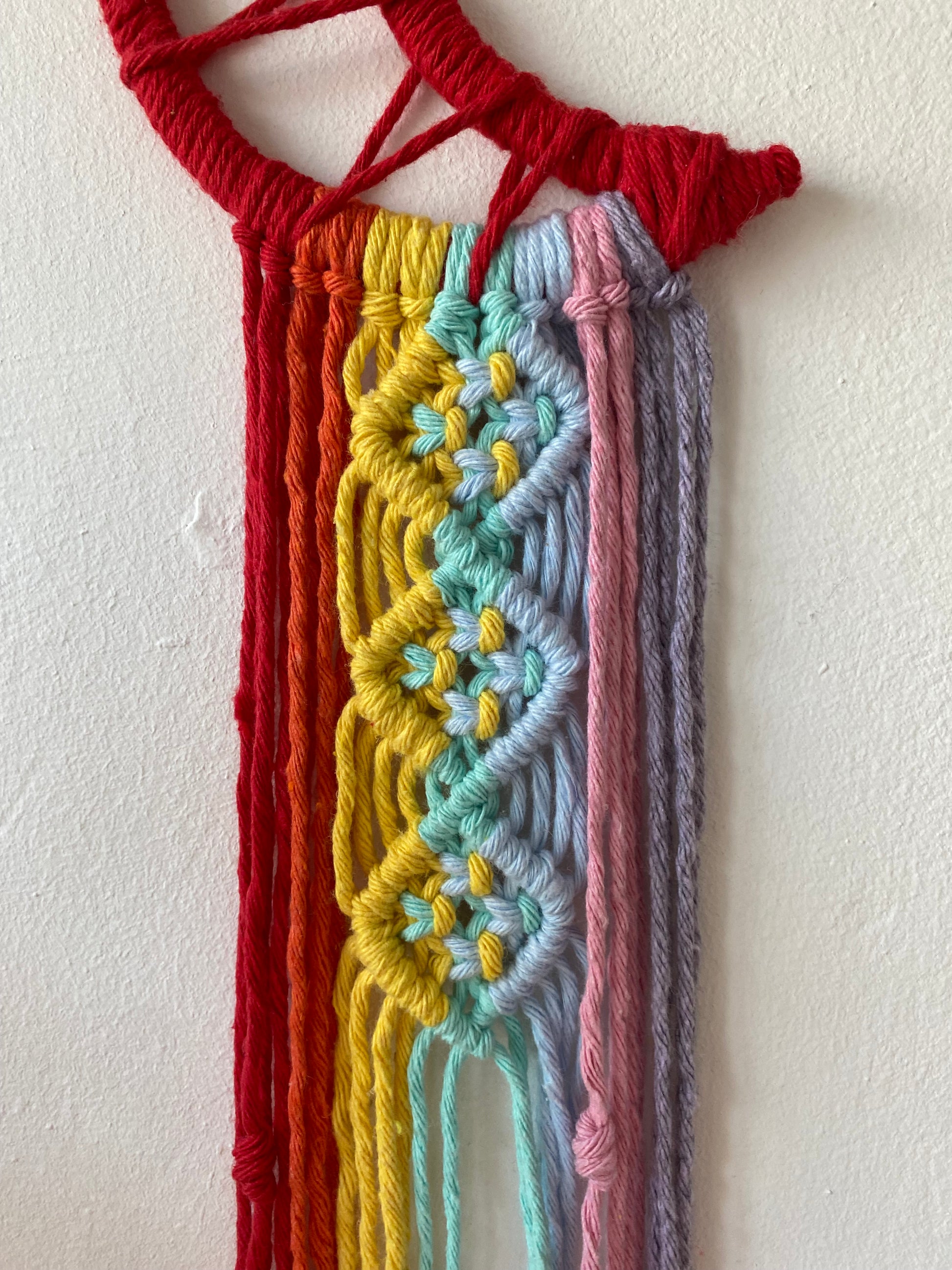 Close up of the intricate knot pattern on a macrame wall hanging made with rainbow colours of cotton yarn.