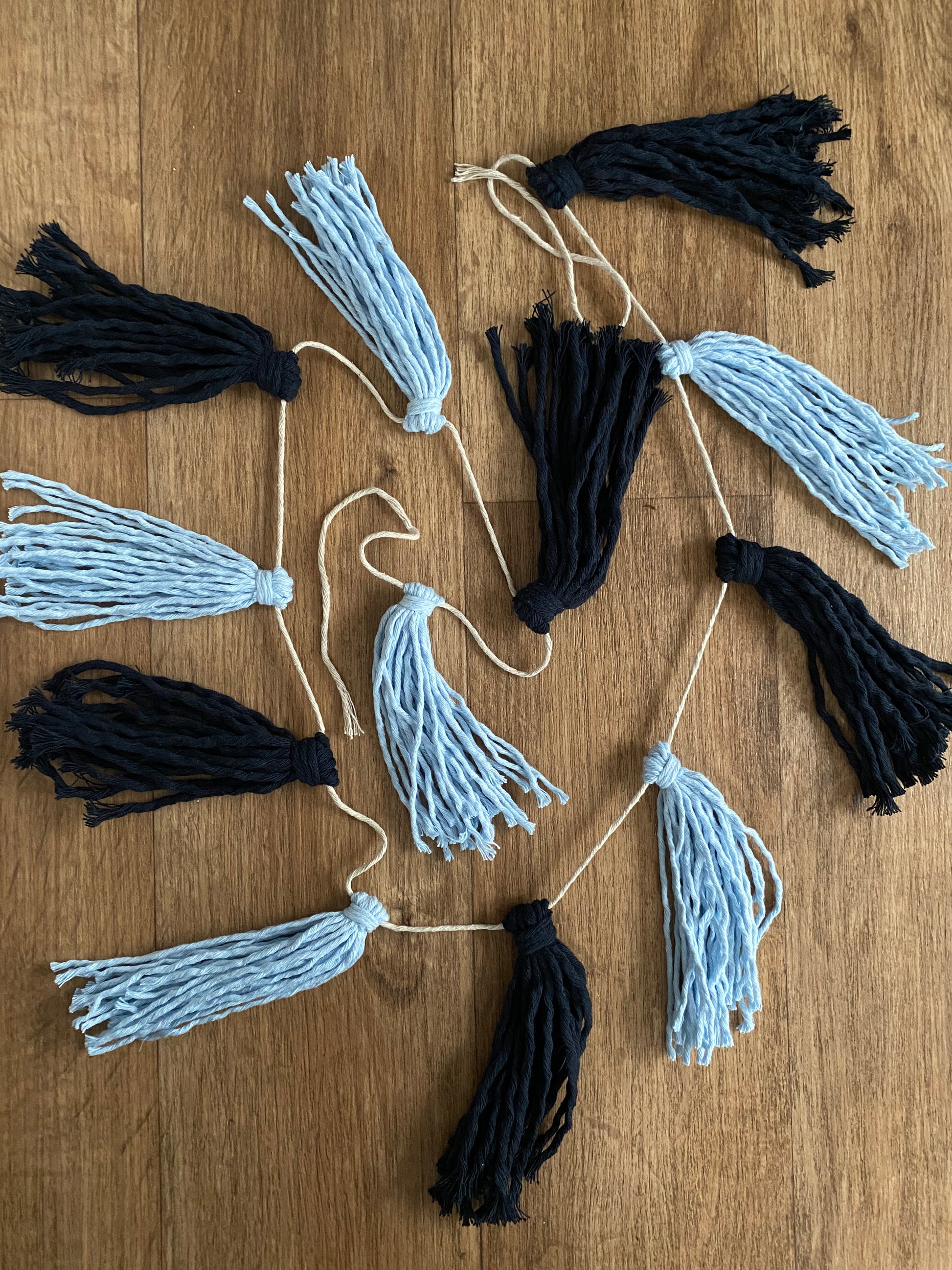 Macrame tassel garland, in shades of blue, laid out on a wooden floor.