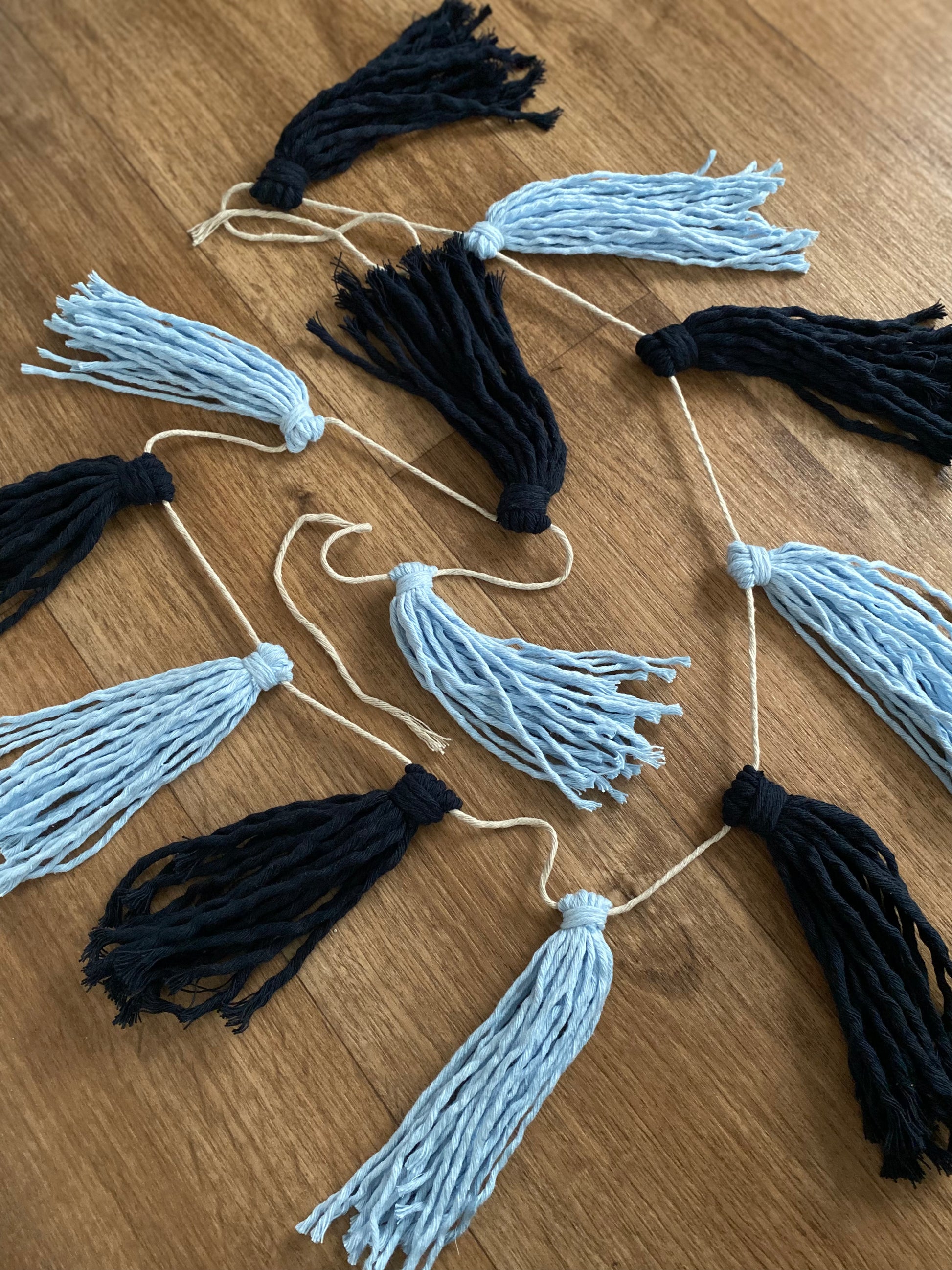 Macrame tassel garland, in shades of blue laid in a circle on a wooden floor.