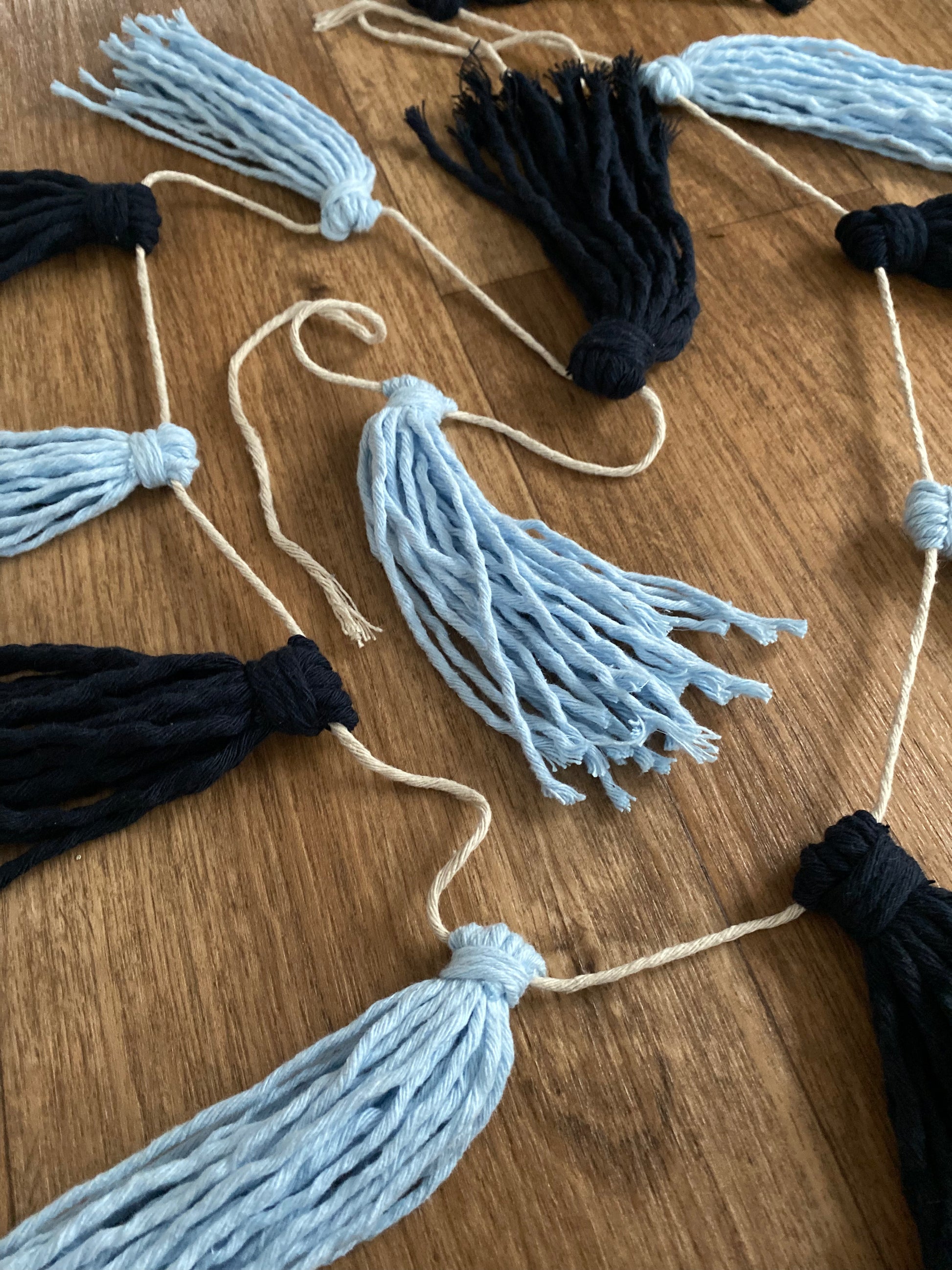 Close up of a macrame tassel garland, in shades of blue laid out on a wooden floor.
