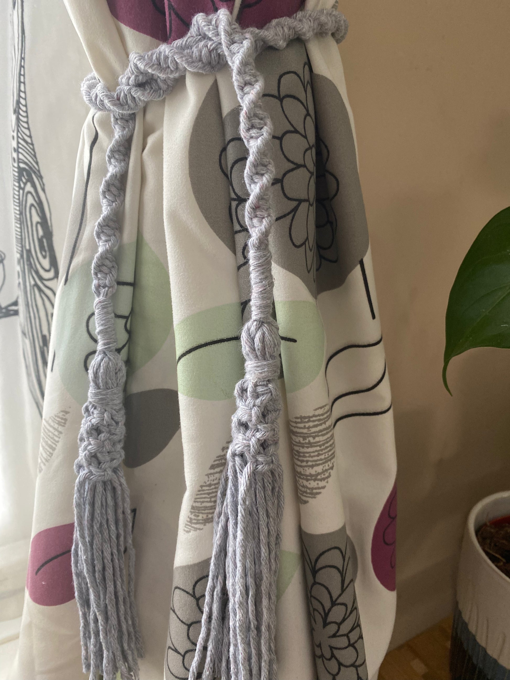 A homely scene featuring patterned curtains held back by knotted macrame tassel tiebacks made with light grey yarn.