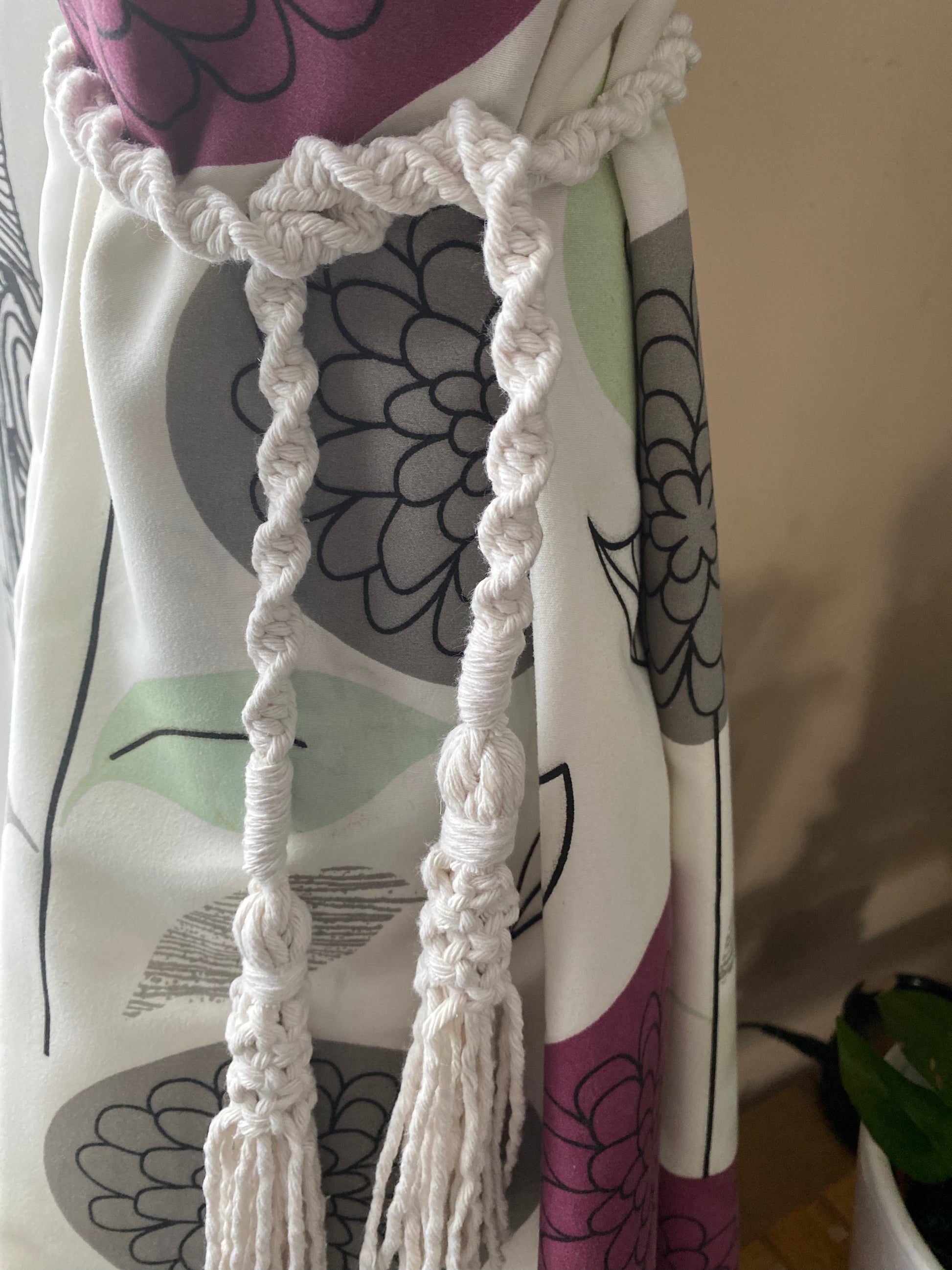 A close up of patterned curtains held back by knotted macrame tassel tiebacks, made with natural yarn.